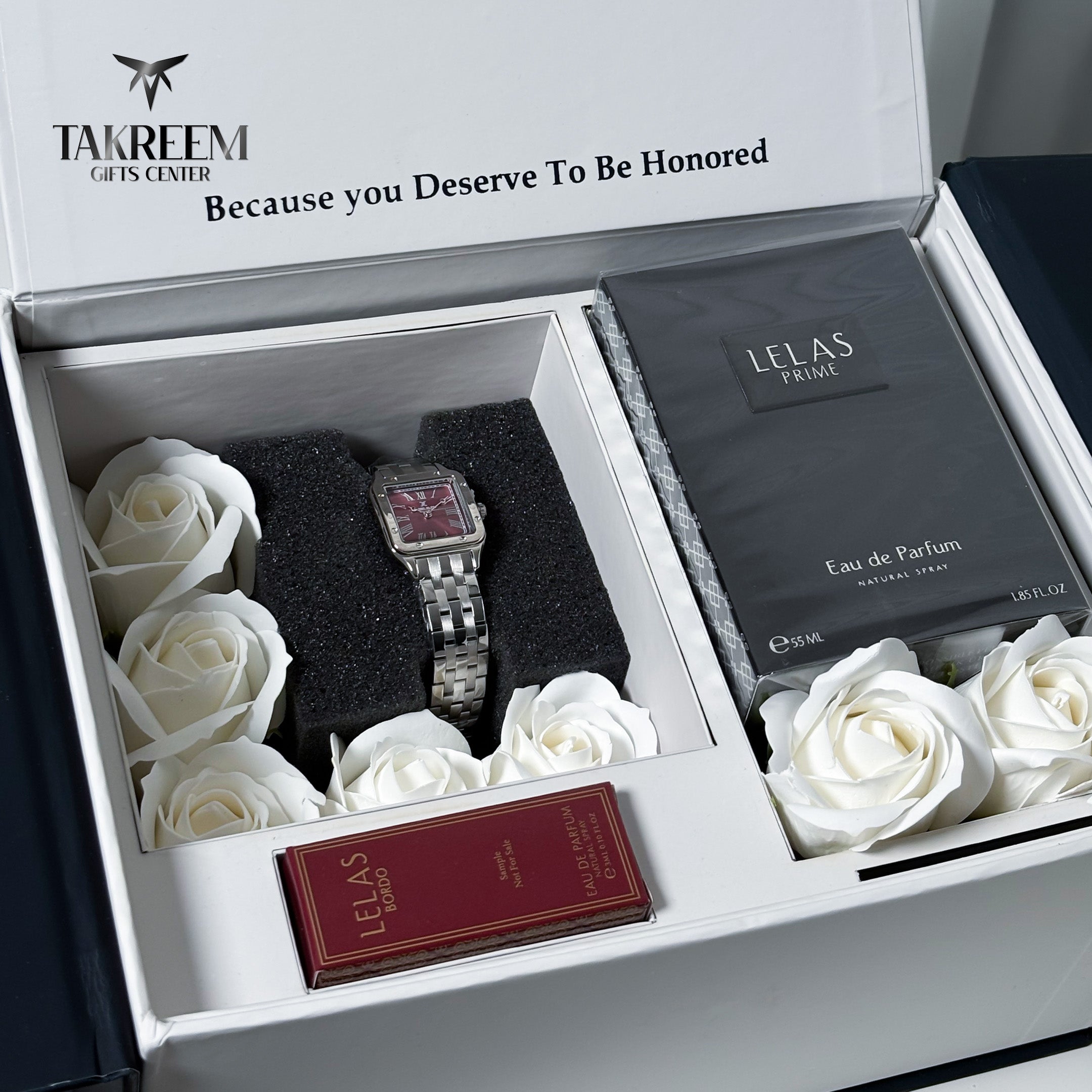 An open luxury gift box from Takreem Gifts Center featuring a silver-toned rectangular watch with a pink face on black foam, white roses, a dark gray Lelas Paris Eau de Parfum bottle, and a small red Lelas Paris box. The inside lid reads 'Because you Deserve To Be Honored'.