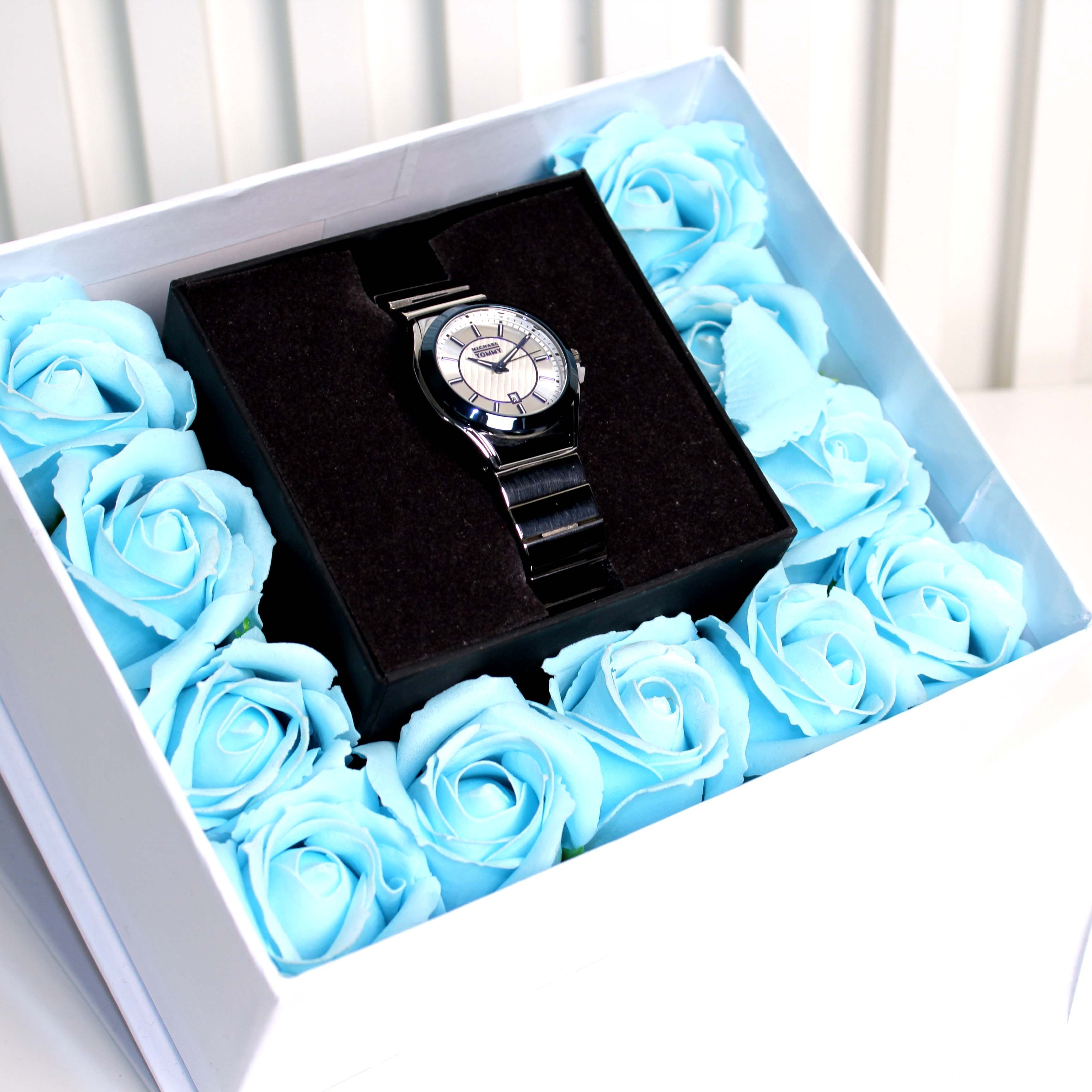 Watch in a black box surrounded by blue roses inside a white box.