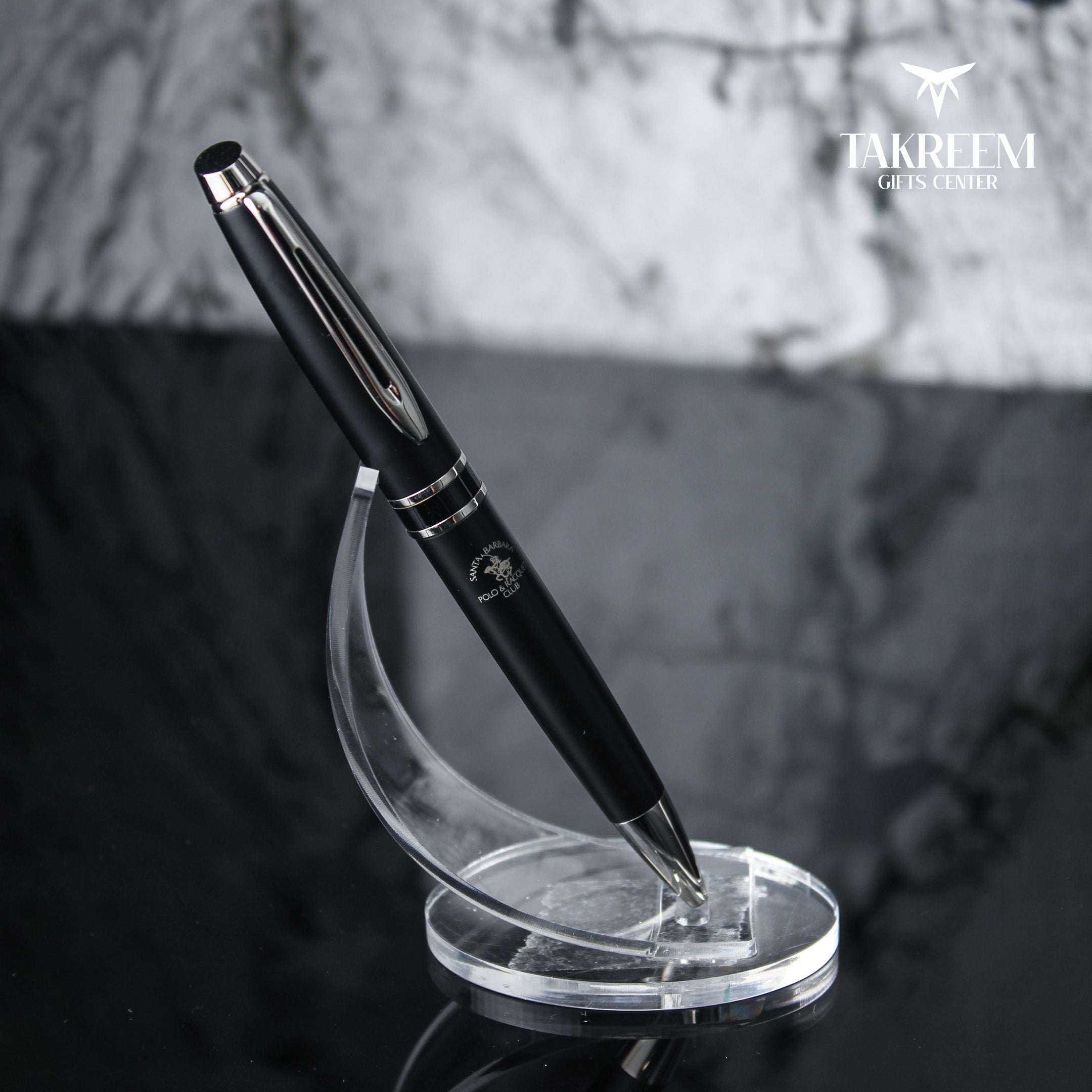 Black pen on a clear stand with a blurred background and 'Takreem Gifts Center' branding.
