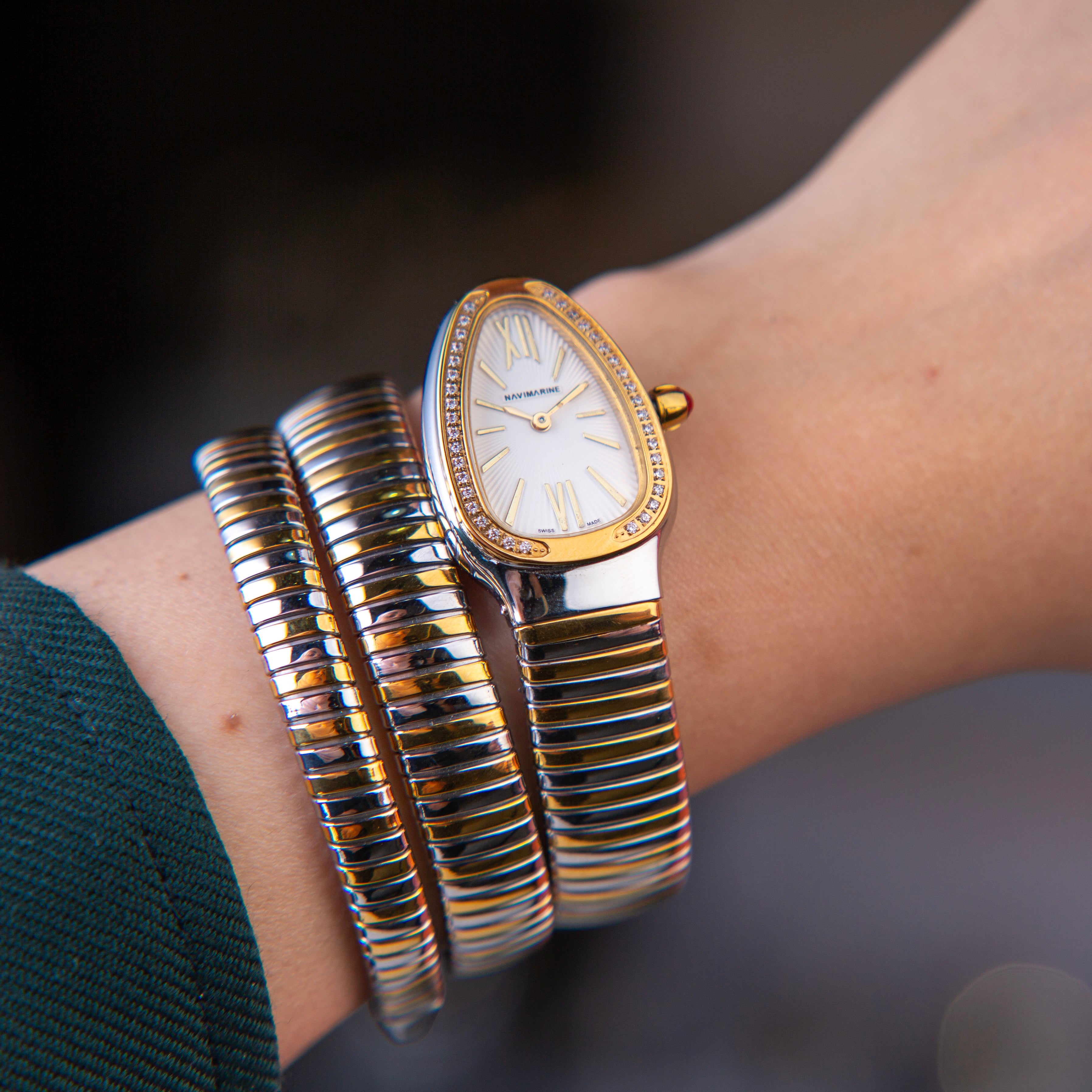 Gold watch and bracelets on a wrist with a blurred background