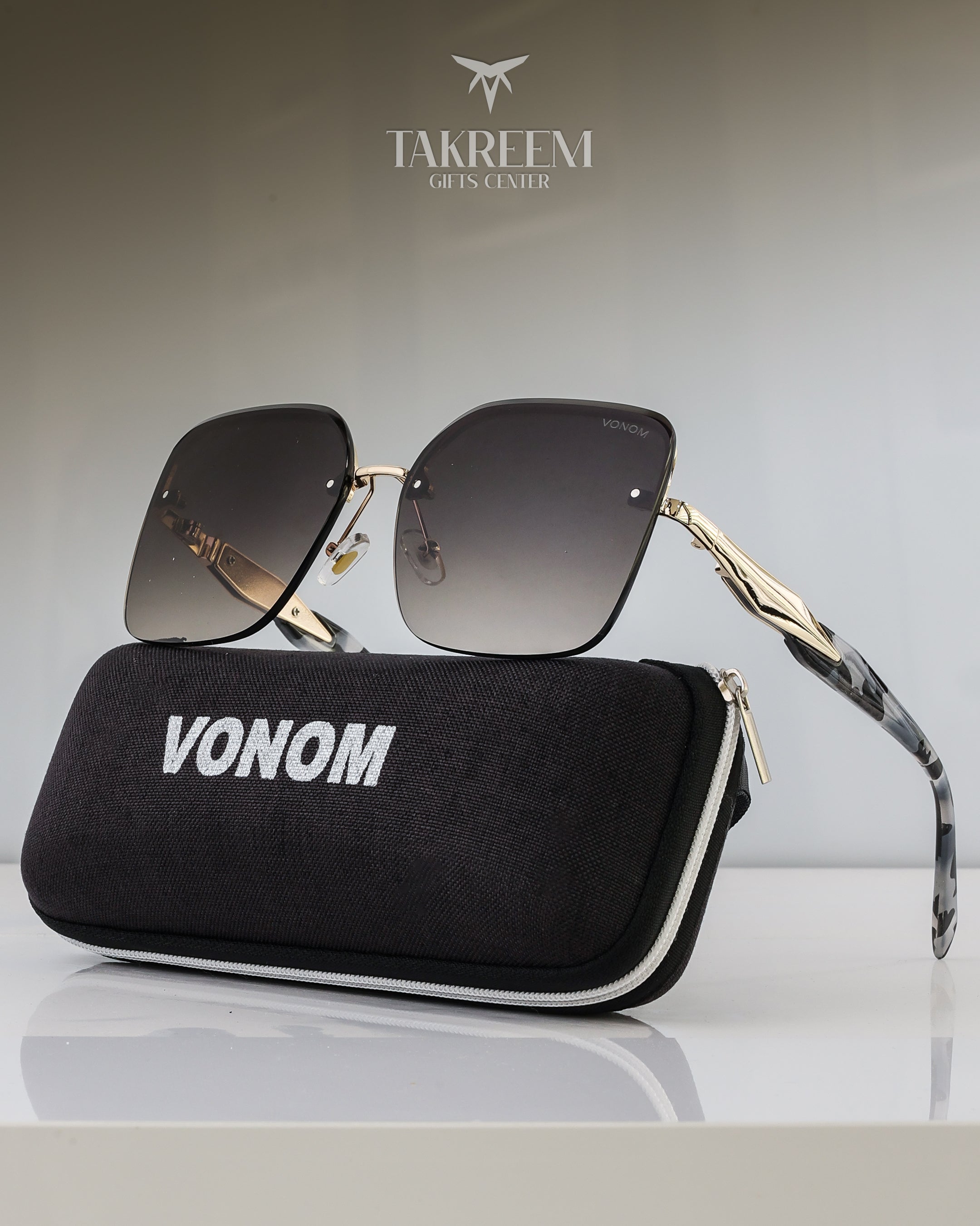 Sunglasses with gold frame and black lenses on a black case labeled 'VONOM' with 'Takreemi Gifts & Center' branding.