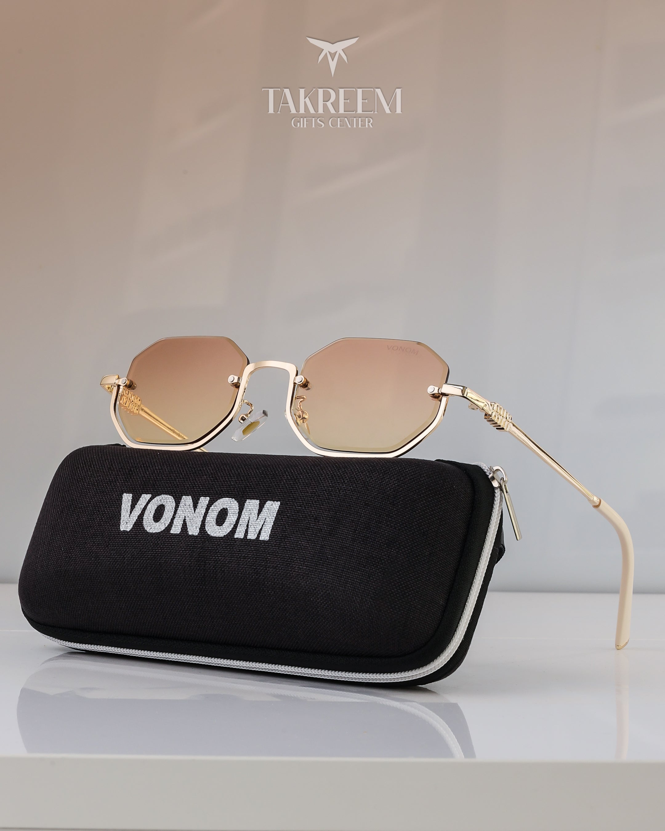 Gold sunglasses with a black case labeled 'VONOM' on a light gray background, featuring the brand 'Takreem'.