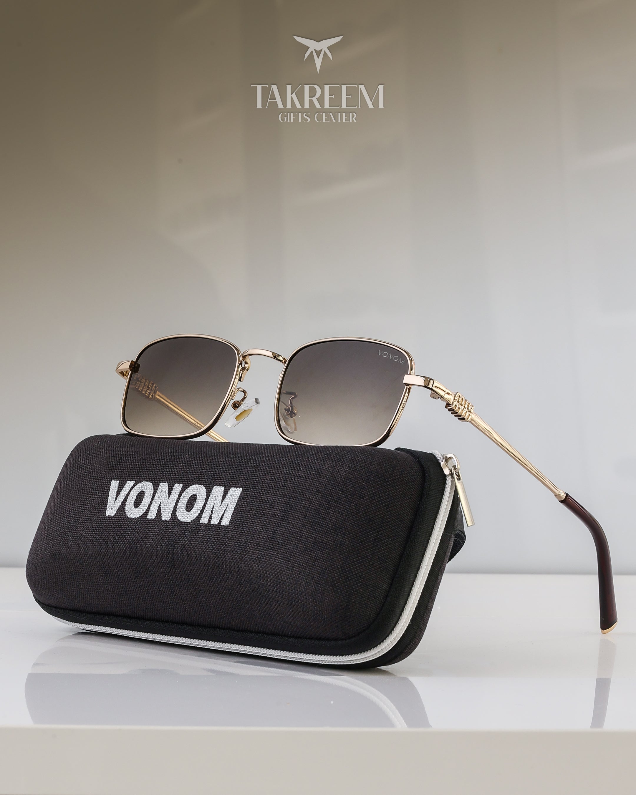 Sunglasses with gold frame and dark lenses on a black case labeled 'VONOM' with 'FAKREEMI' brand in the background.