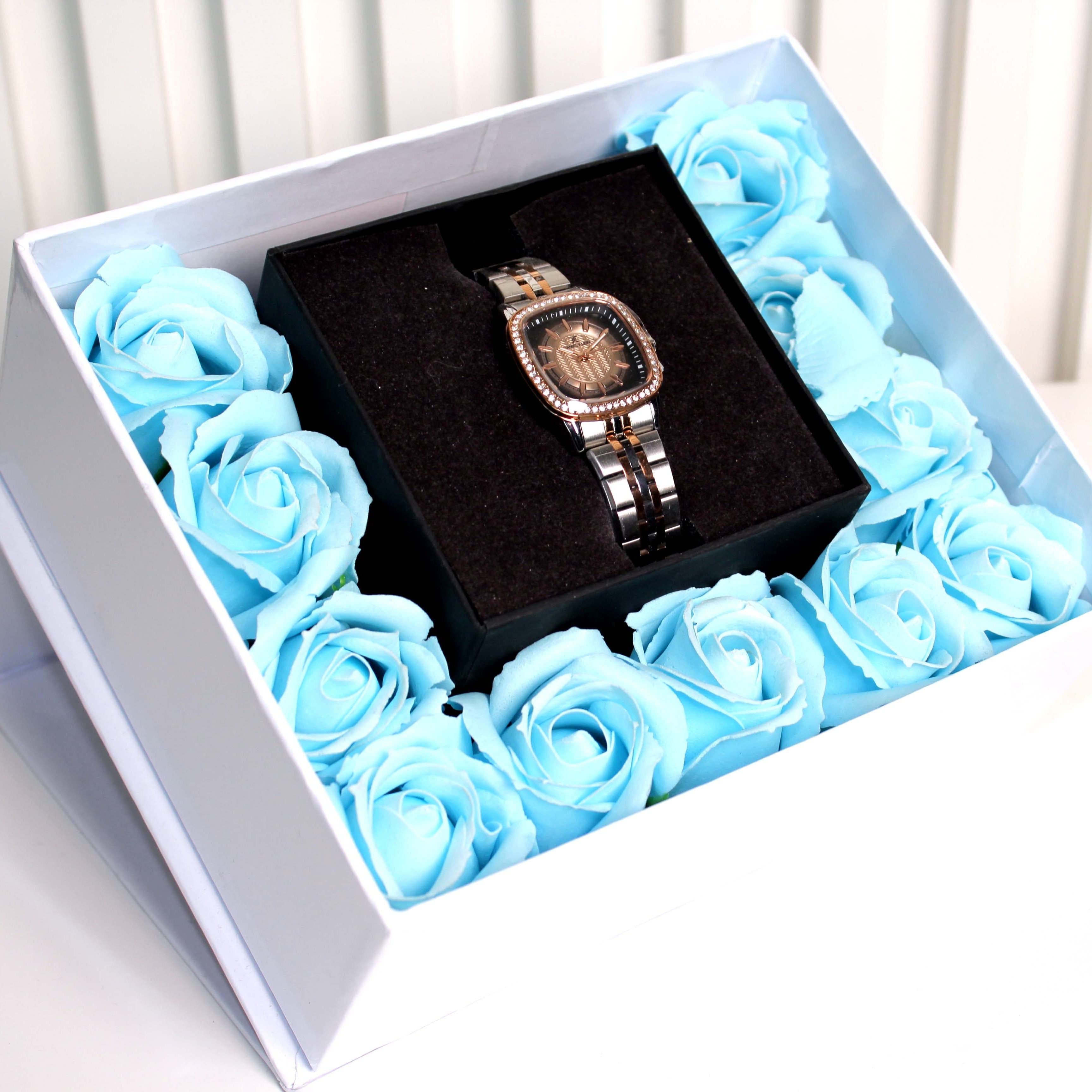 Watch in a box surrounded by blue roses on a white surface