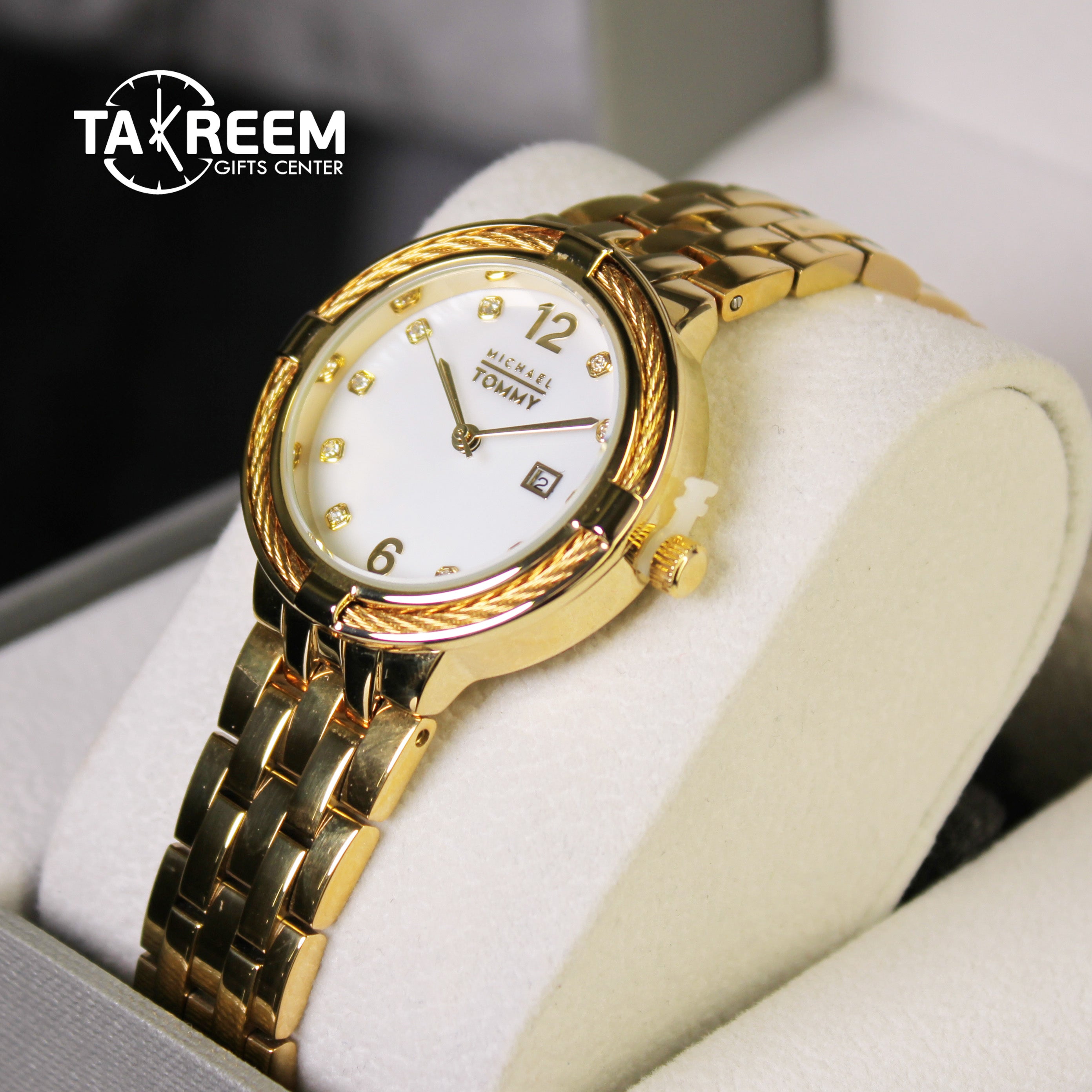 Gold wristwatch with white dial on a white cushion, branded 'Takreem Gifts Center'.
