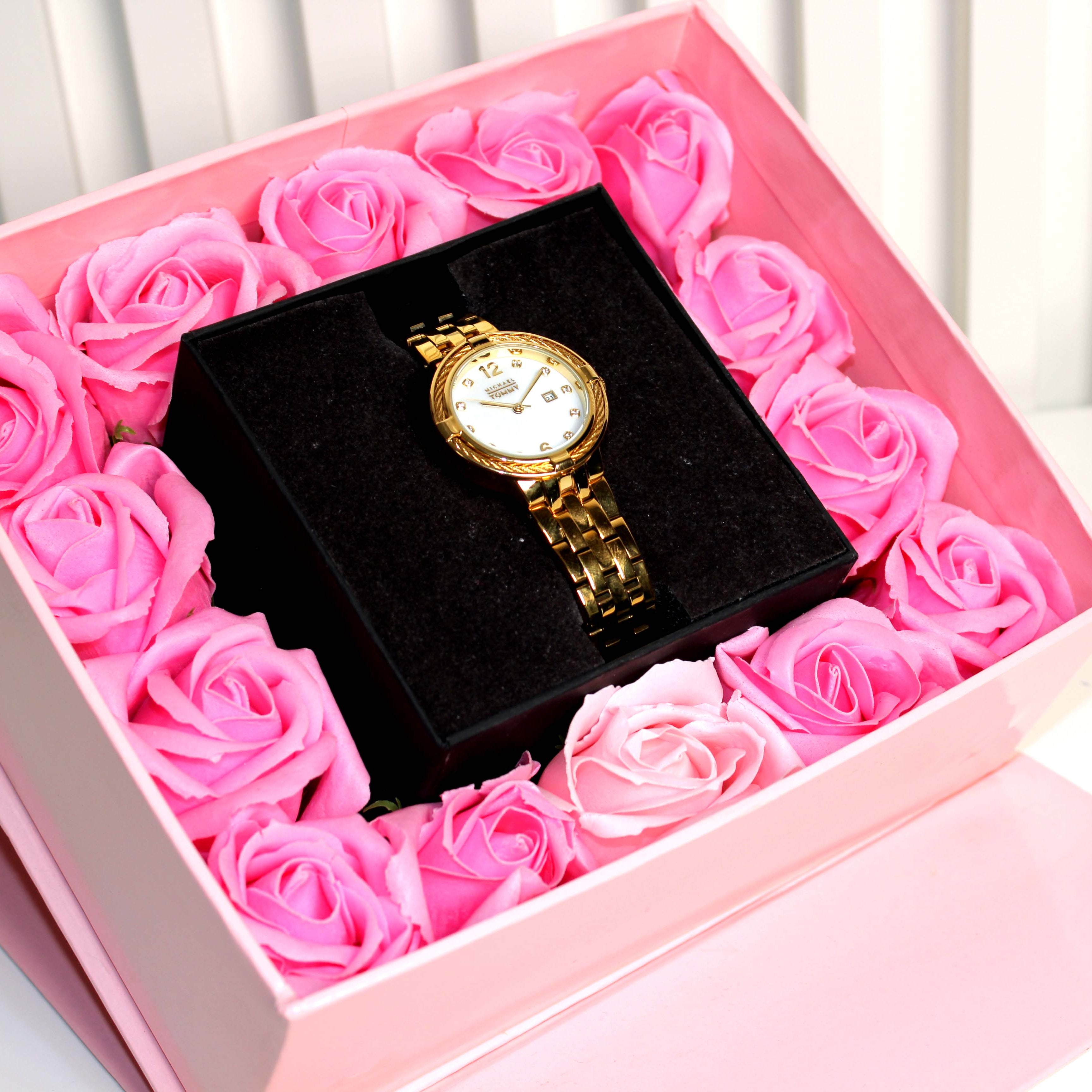 Gold watch in a box filled with pink roses on a white background