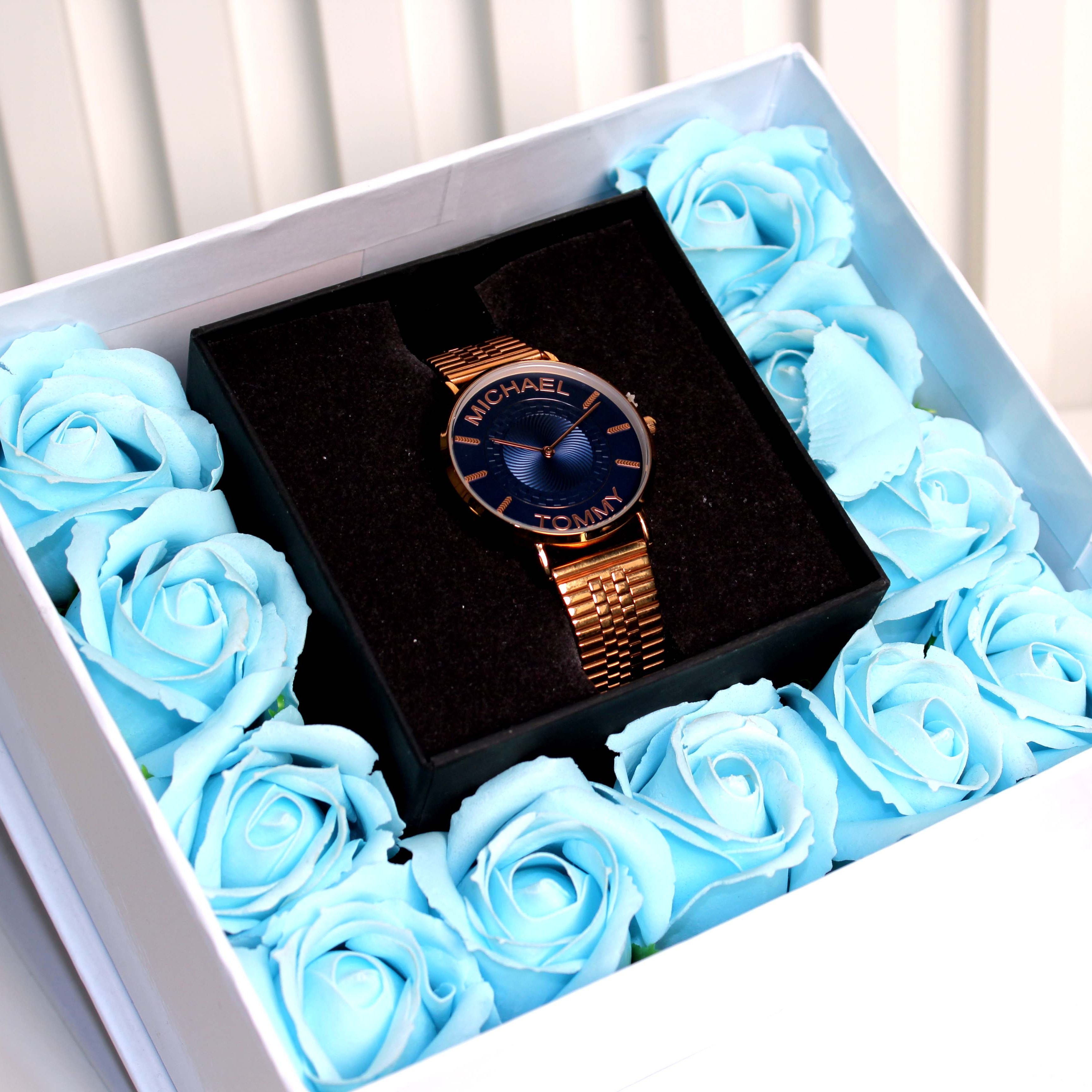 Watch in a box surrounded by blue roses on a white background