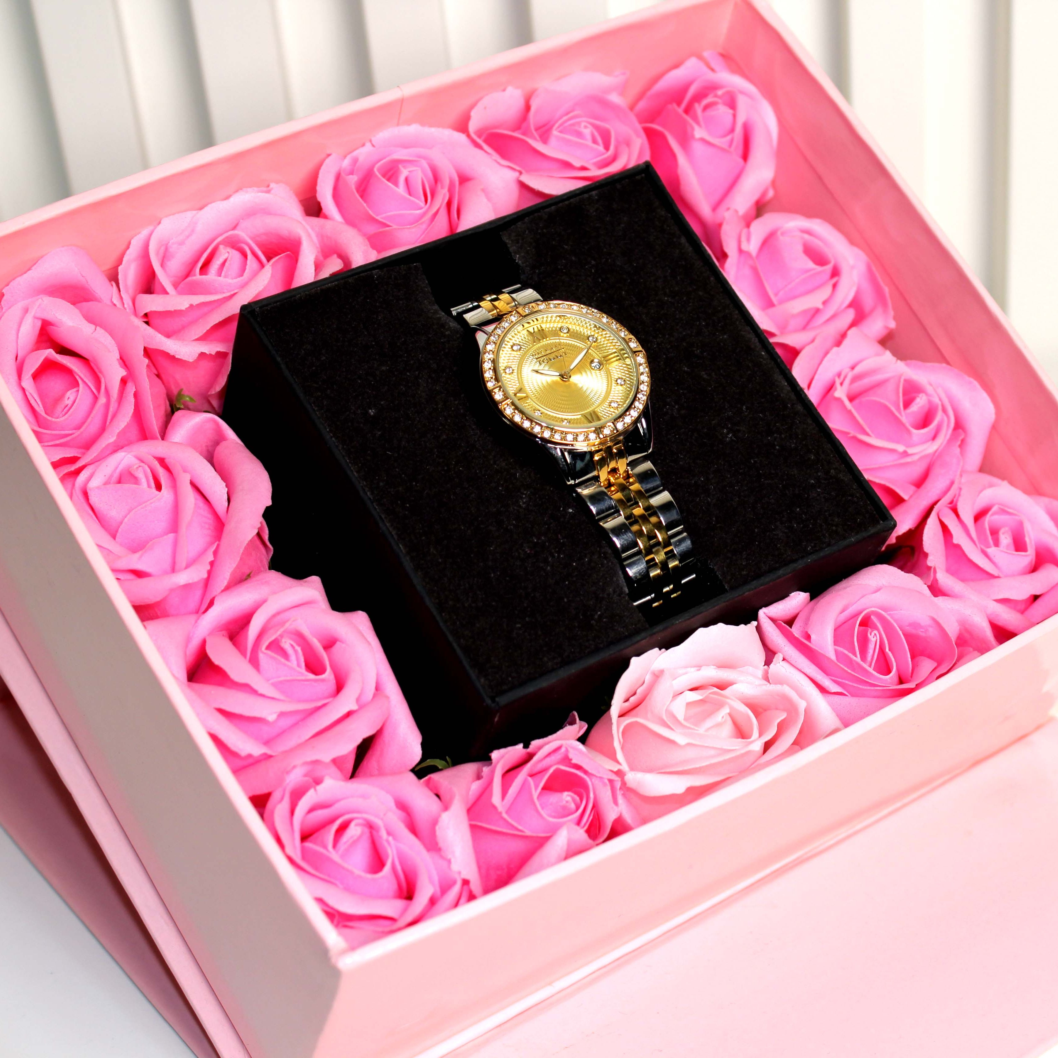 Gold watch in a box surrounded by pink roses
