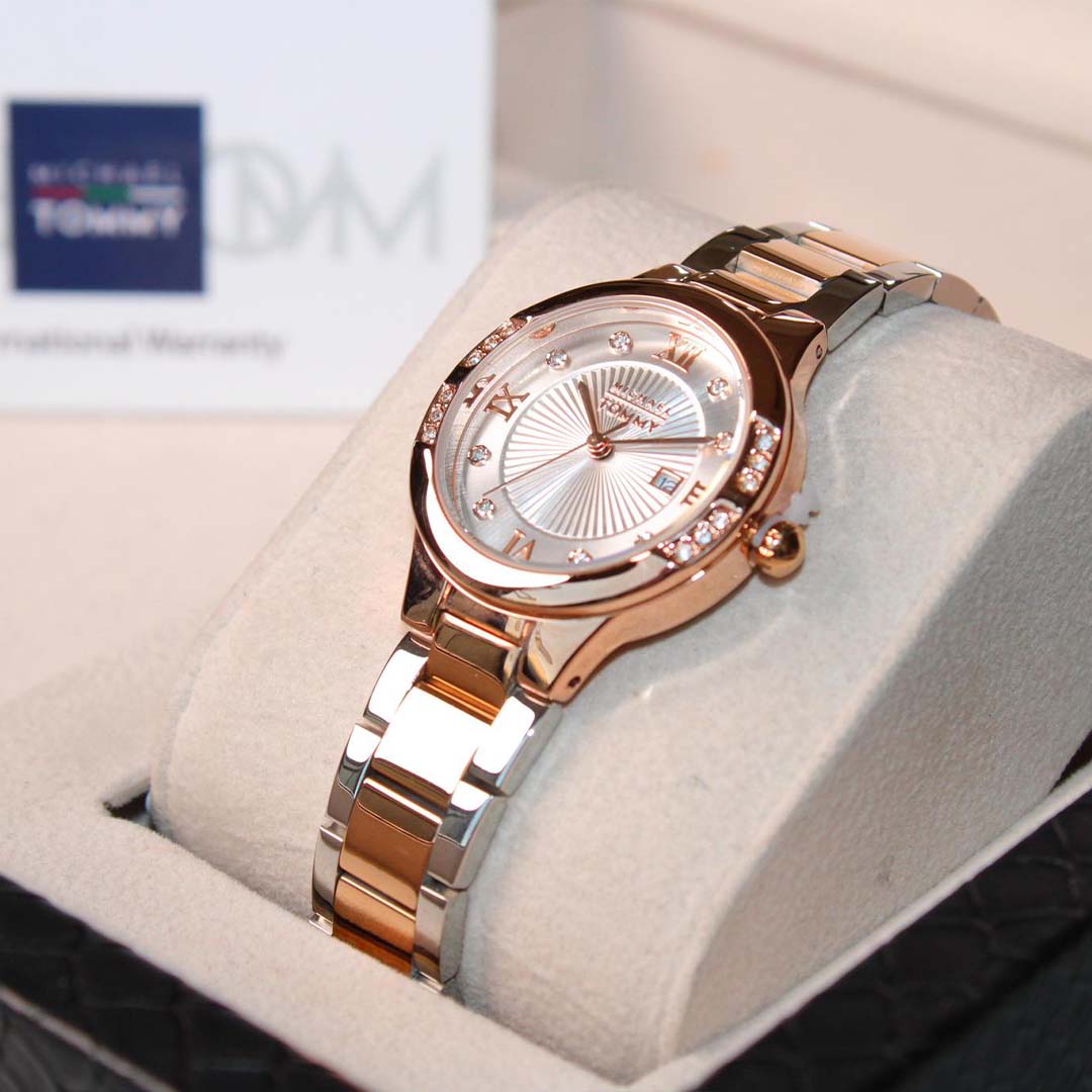Rose gold watch with diamond accents on a white cushion, brand name visible in the background