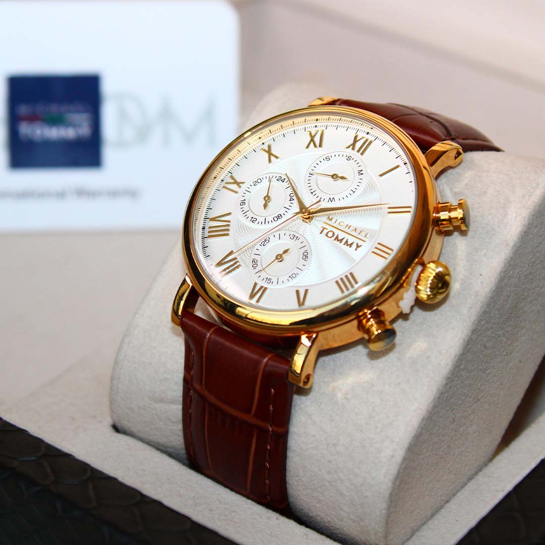 Gold watch with brown leather strap on a white cushion, Tommy Hilfiger logo in the background