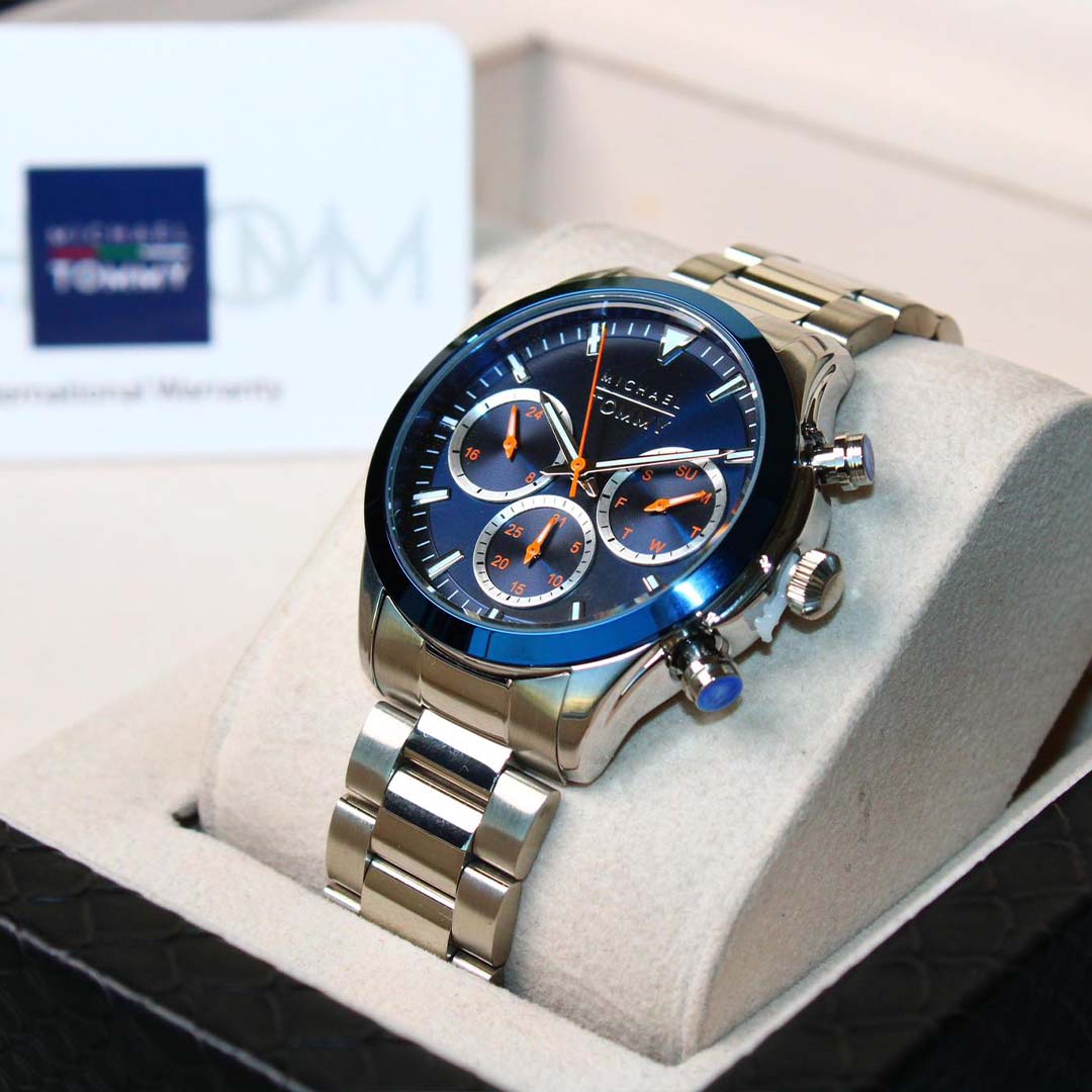 Silver watch with blue face in a display case, Tommy Hilfiger box in the background