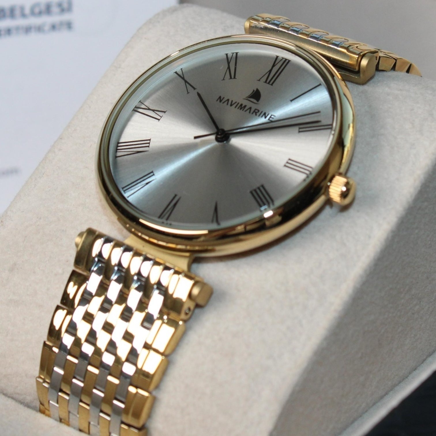 Gold wristwatch with silver face on a light gray cushion