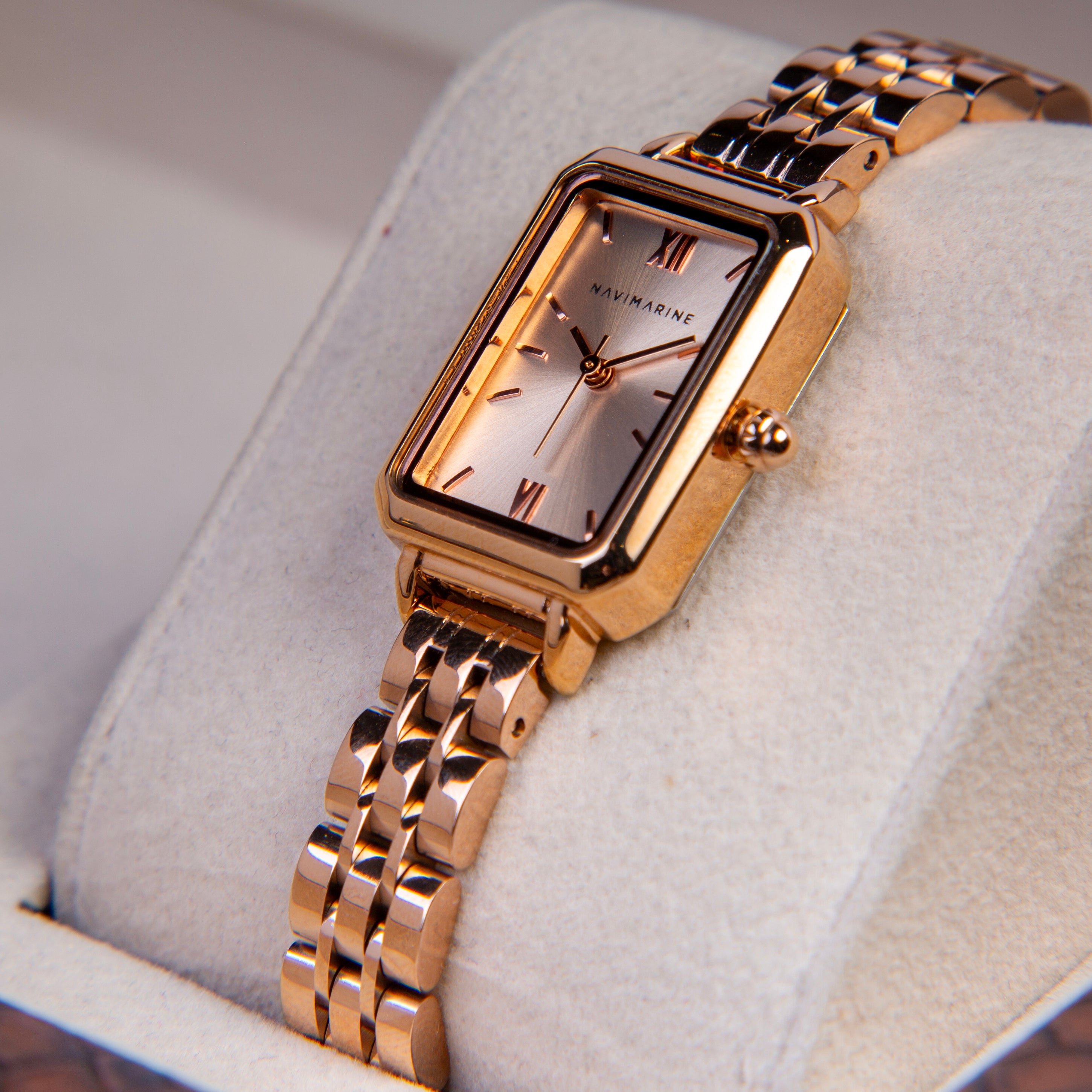 Rose gold watch with a white face on a light gray cushion