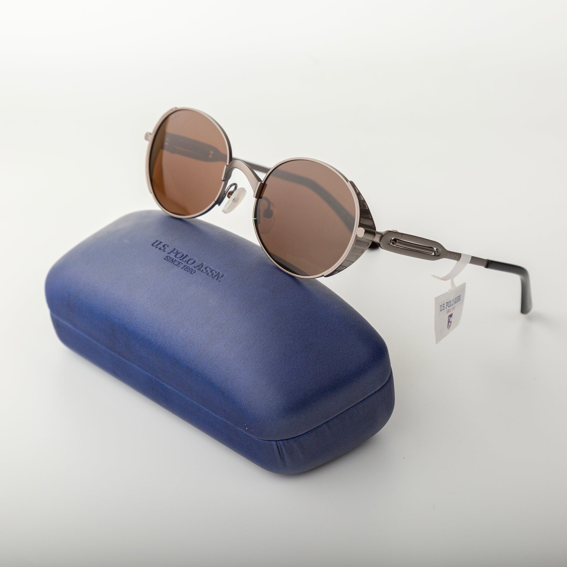 Round sunglasses with brown lenses and metal frame on a blue case against a white background