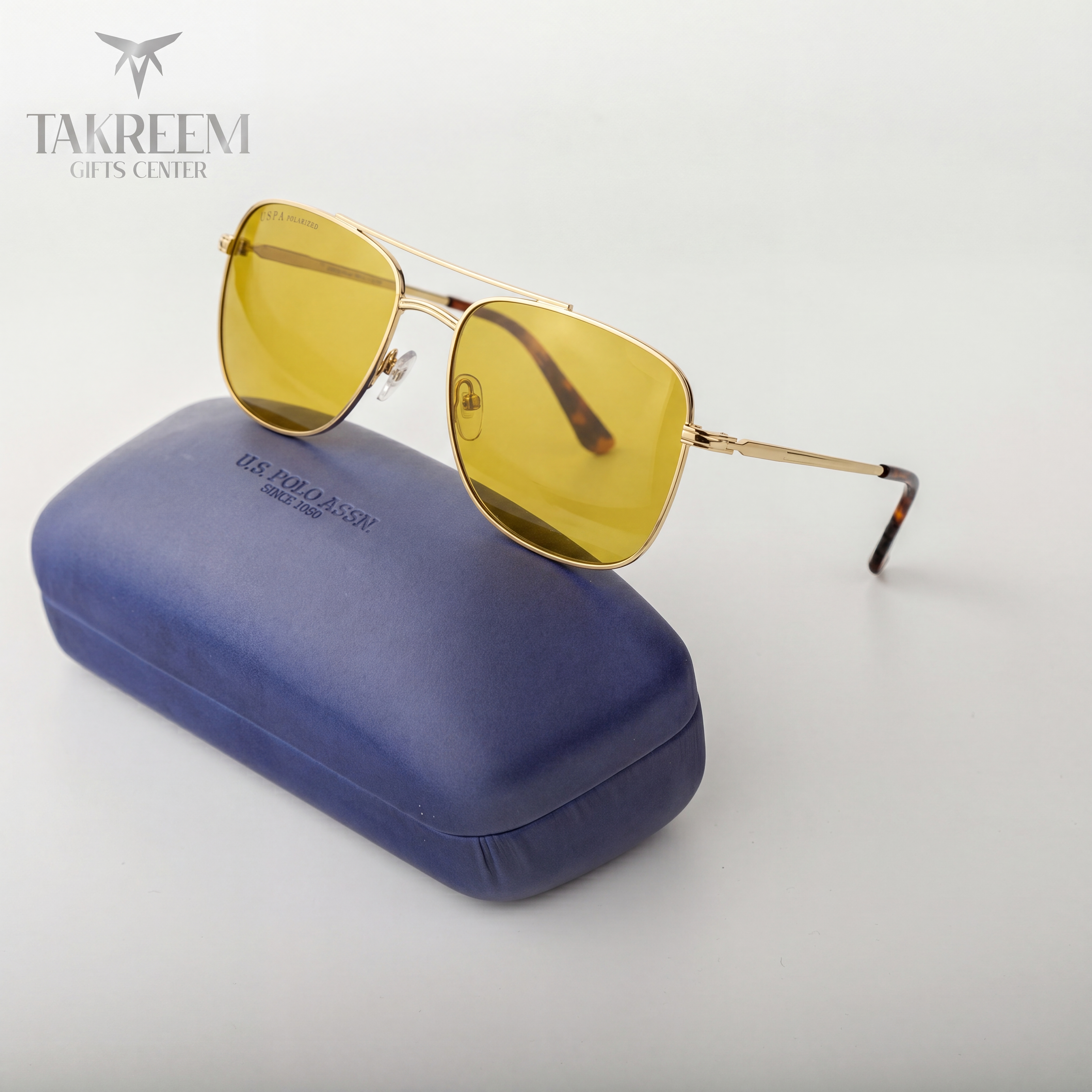 Gold-framed sunglasses with yellow lenses on a blue case, branded 'Takreem Gifts Center'.