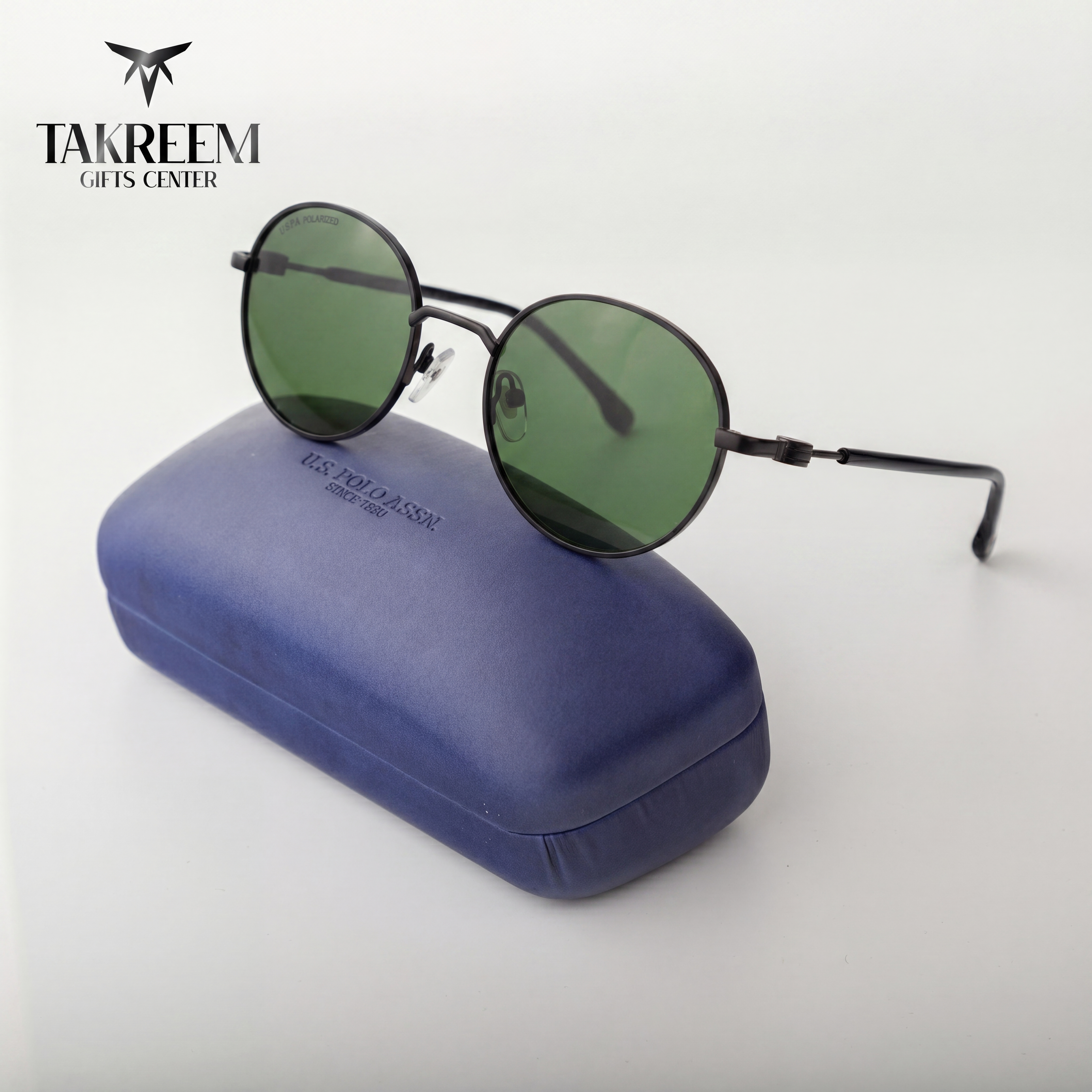 Round sunglasses with green lenses on a blue case, branded 'Takreem Gifts Center'.