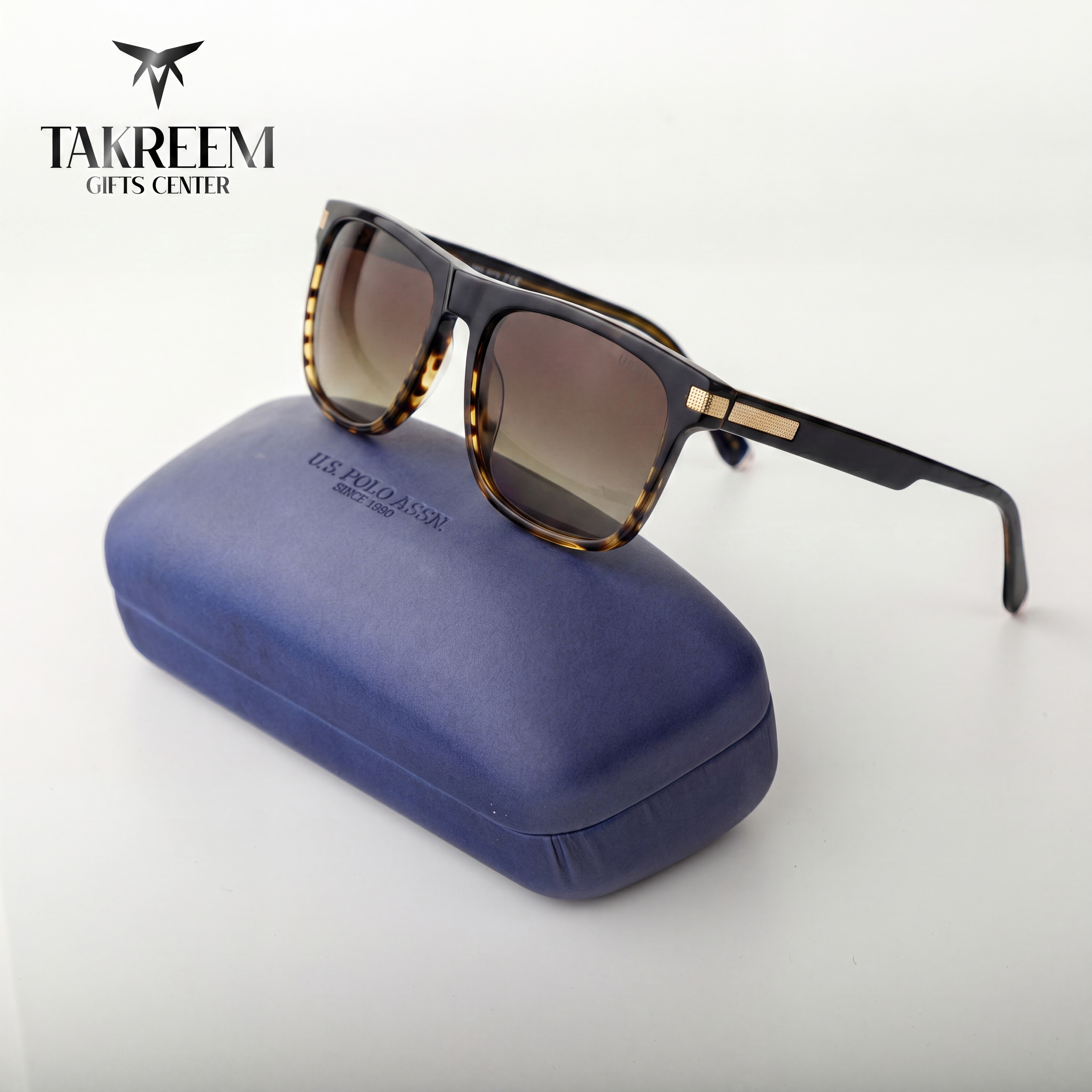 Sunglasses with tortoiseshell frame and brown lenses on a blue case, brand 'Takreem' visible.
