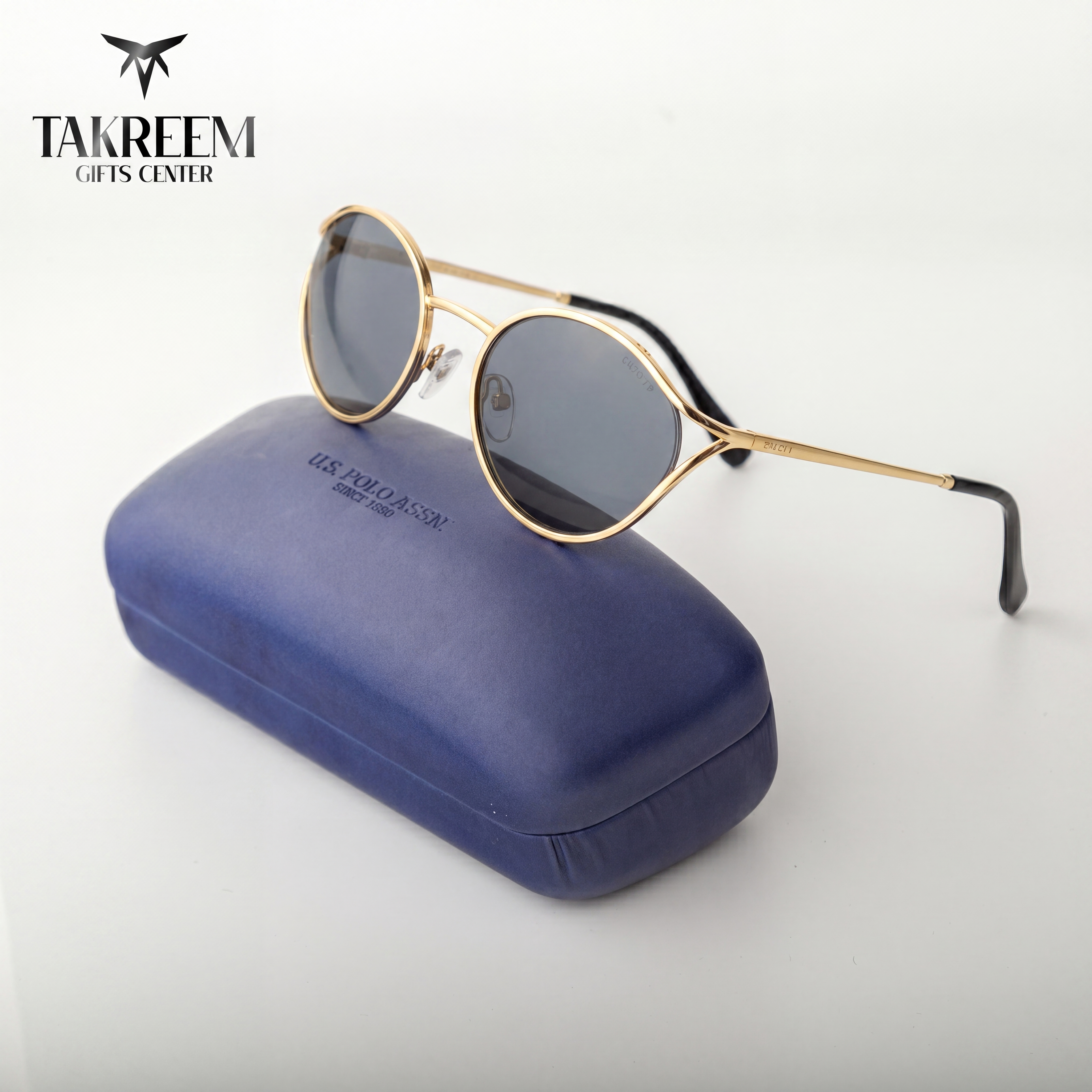 Gold-framed sunglasses on a blue case with 'Takreem Gifts Center' branding.