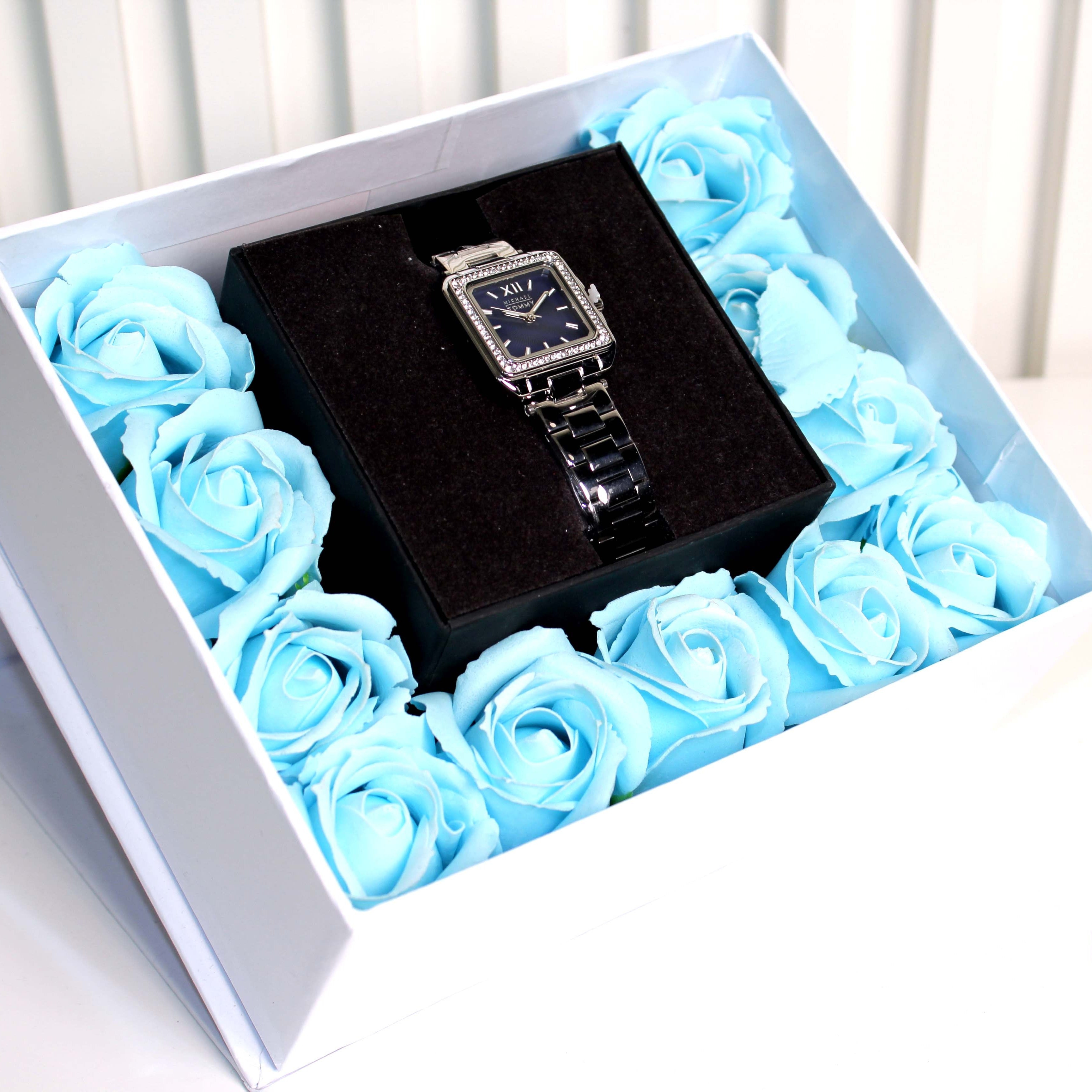 Black watch in a box surrounded by blue roses on a white surface