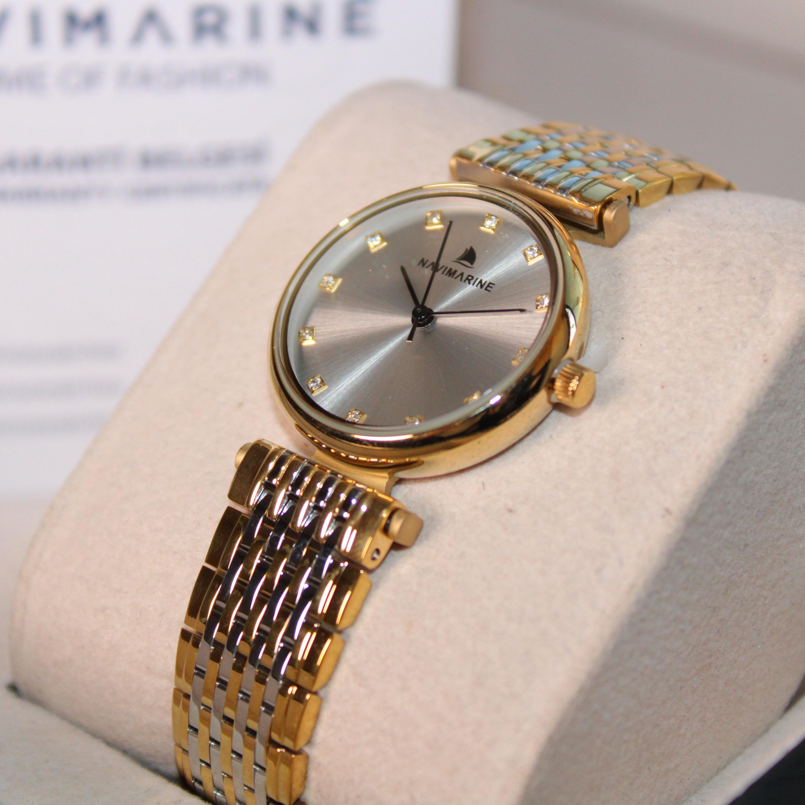 Gold wristwatch on a display stand with 'Navimagine' branding in the background.