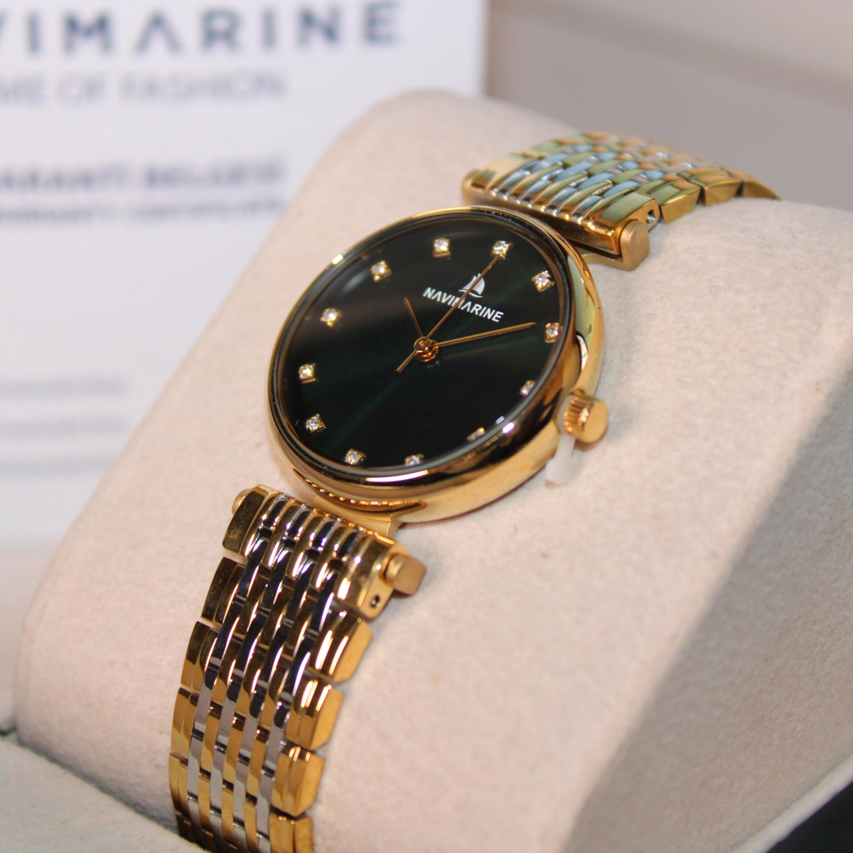 Gold wristwatch with black face on a display stand, brand 'Navimarine' visible