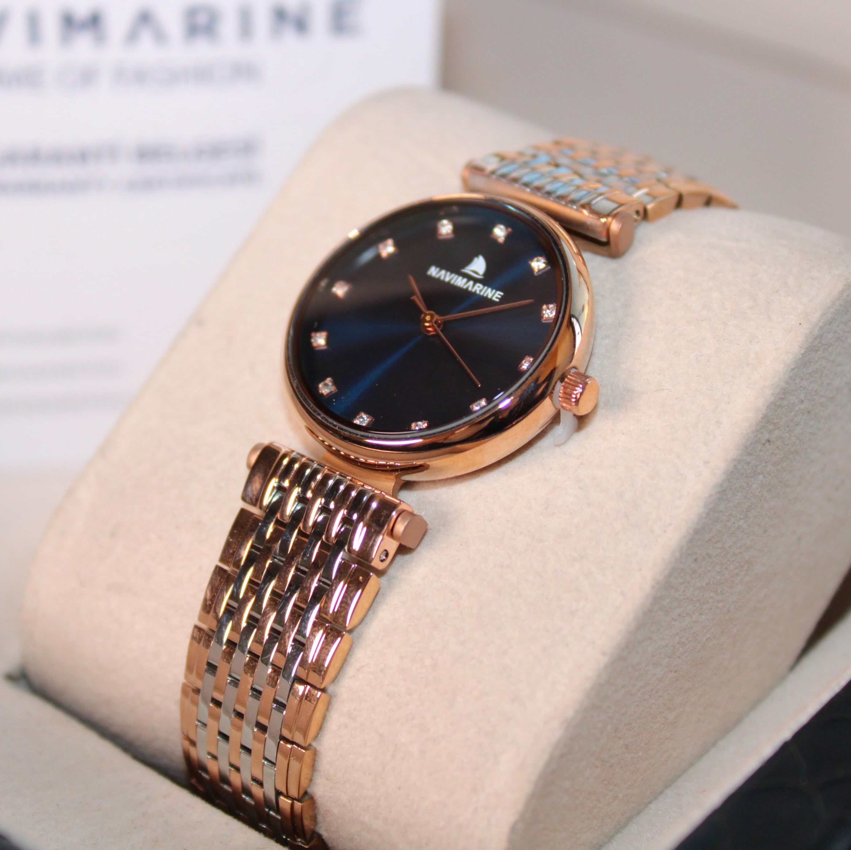 Rose gold watch on a display stand with 'NaviMarine' branding in the background.