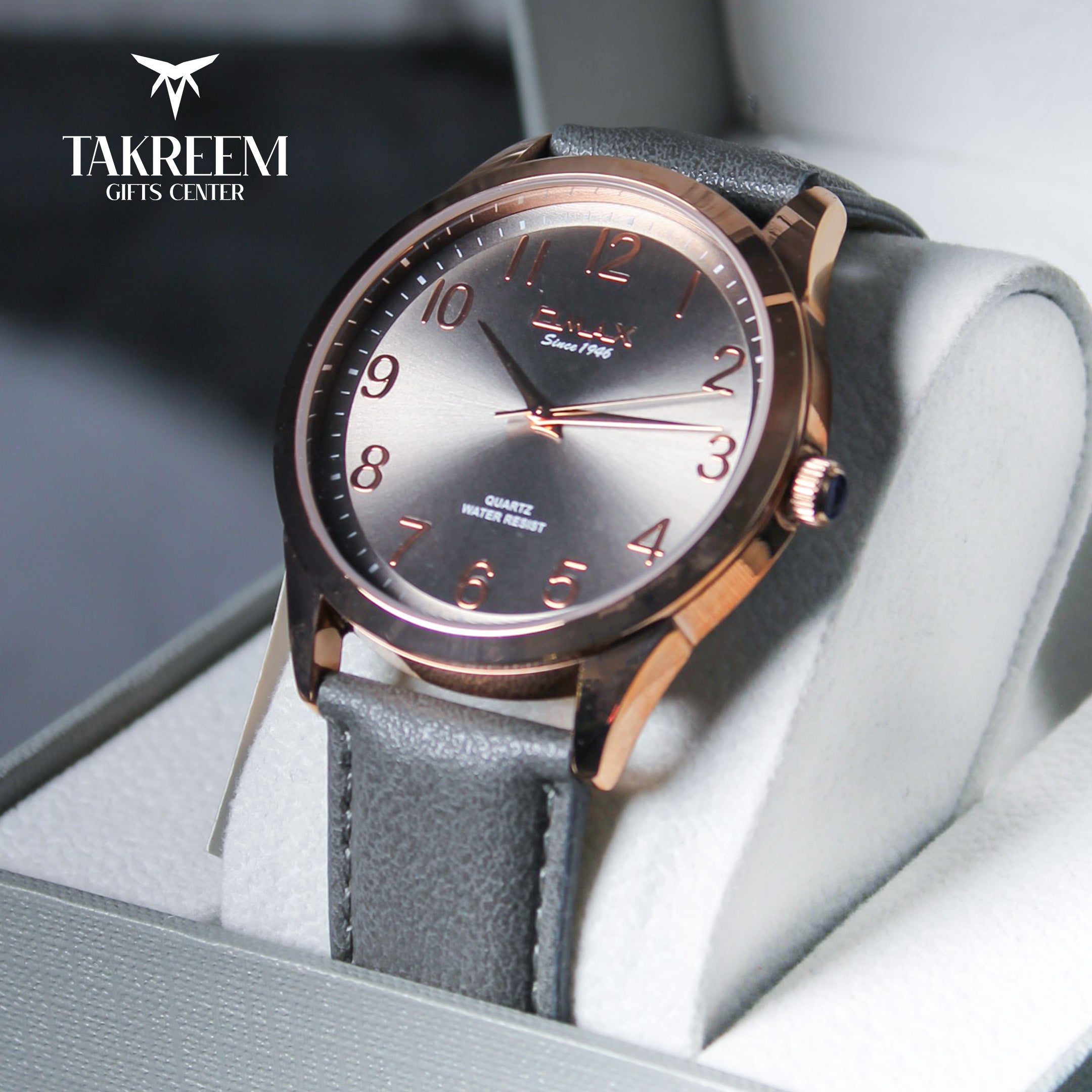 Wristwatch with rose gold case and gray strap on a light gray background, brand 'Takreem' visible.