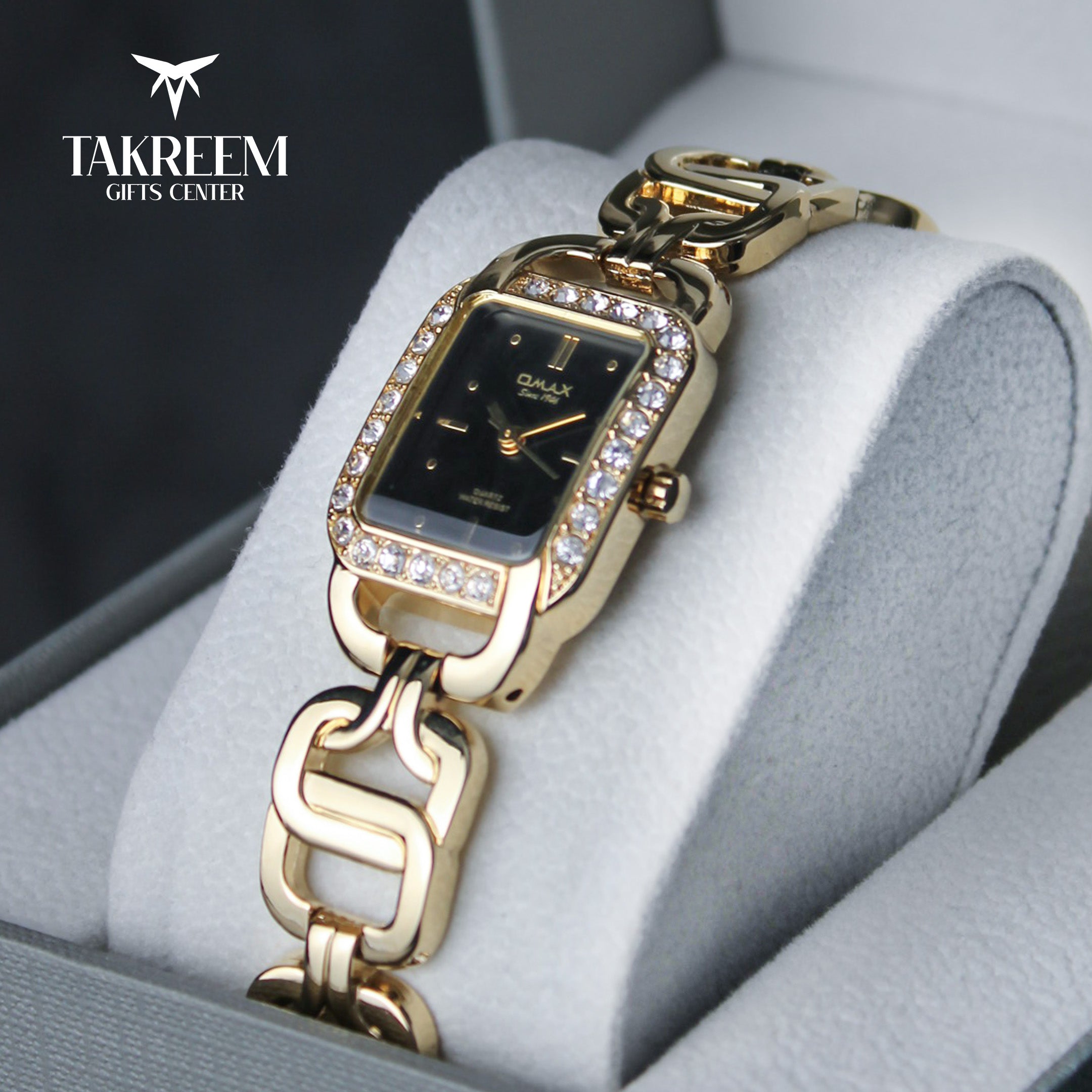 Gold wristwatch with chain design on a gray cushion, branded 'Takreem Gifts Center'.