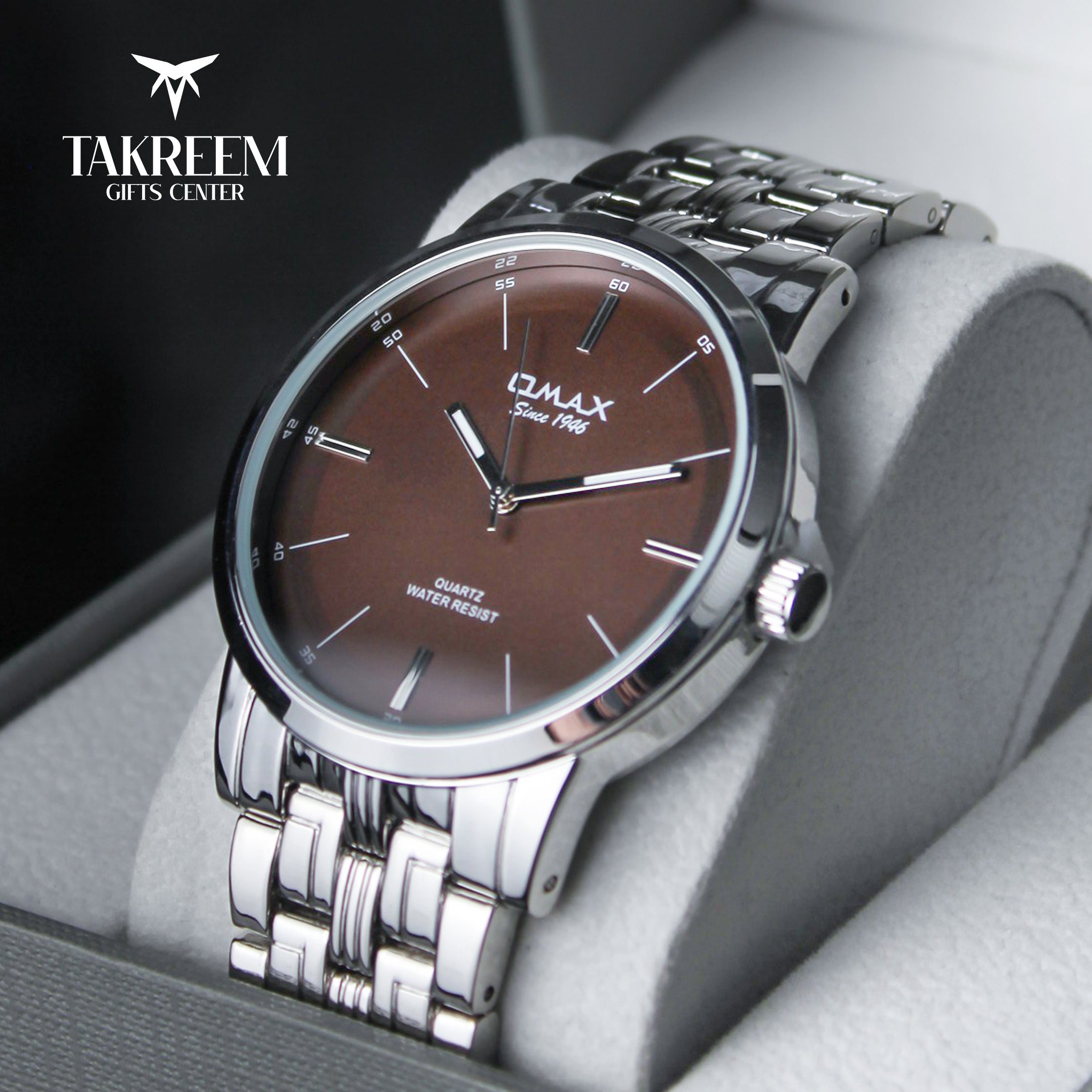 Luxury watch with brown dial and silver metal strap on a gray surface, brand 'Takreem' visible.