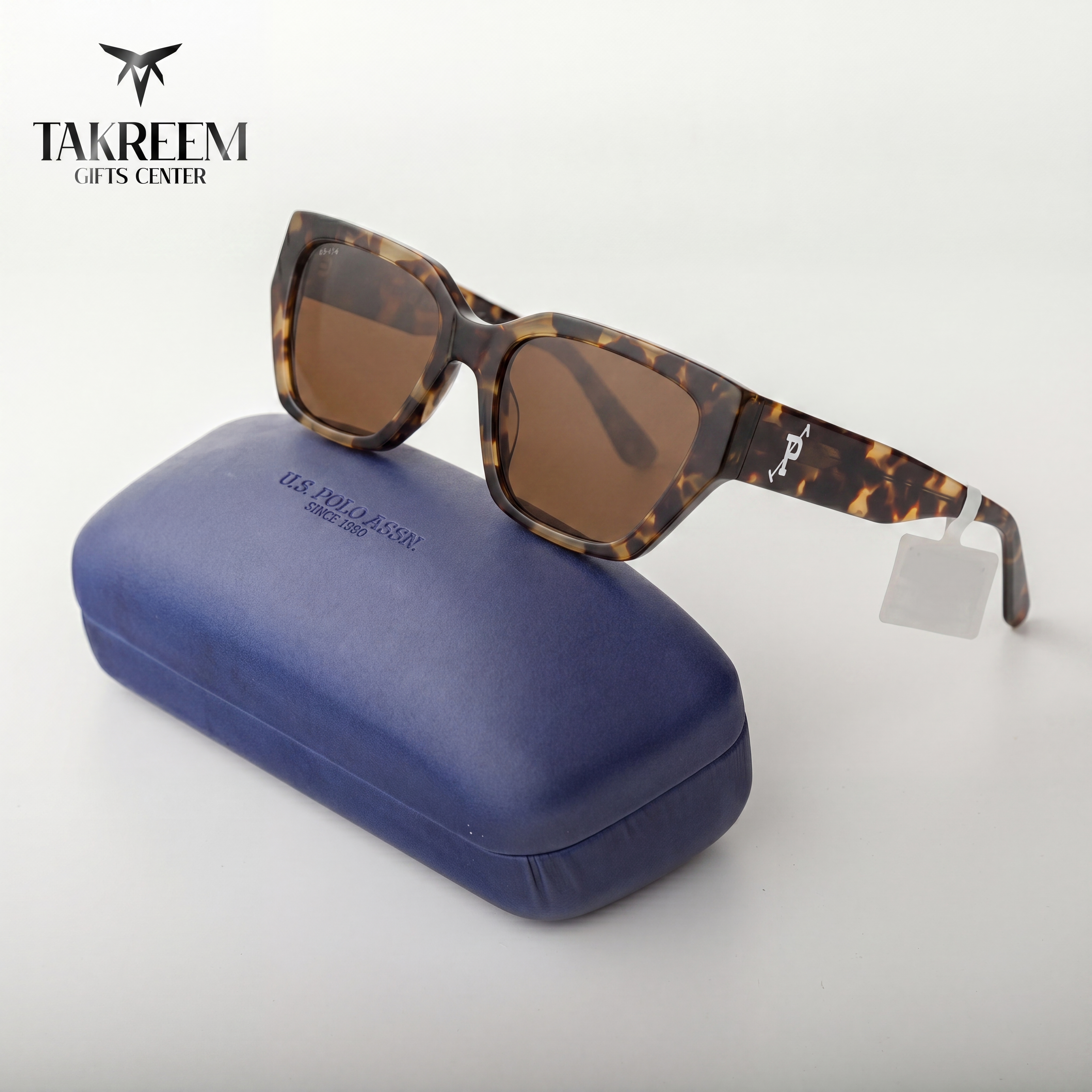 Sunglasses with tortoiseshell frame and brown lenses on a blue case, branded 'Takreem Gifts Center'.