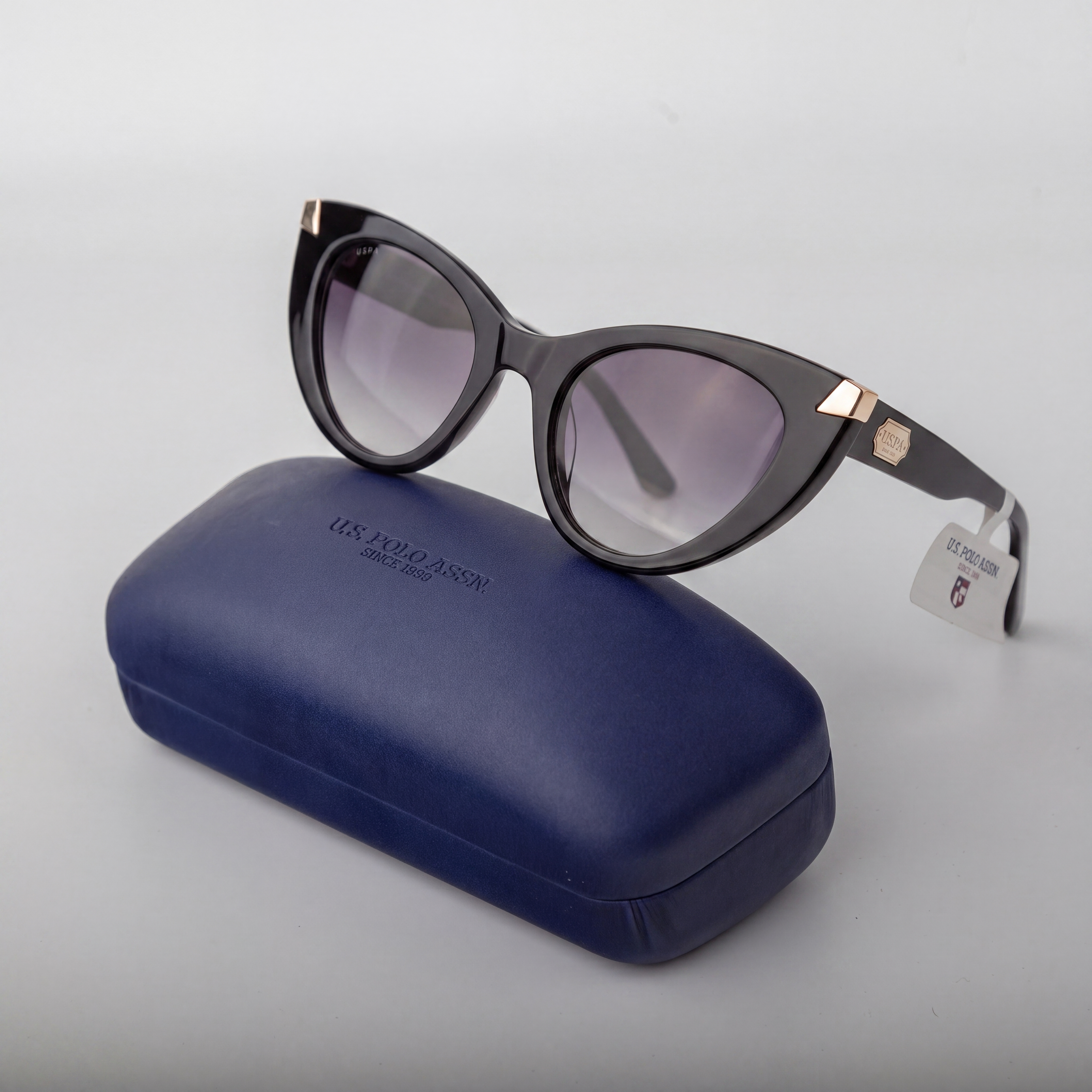 Black sunglasses with purple lenses on a blue case against a light gray background