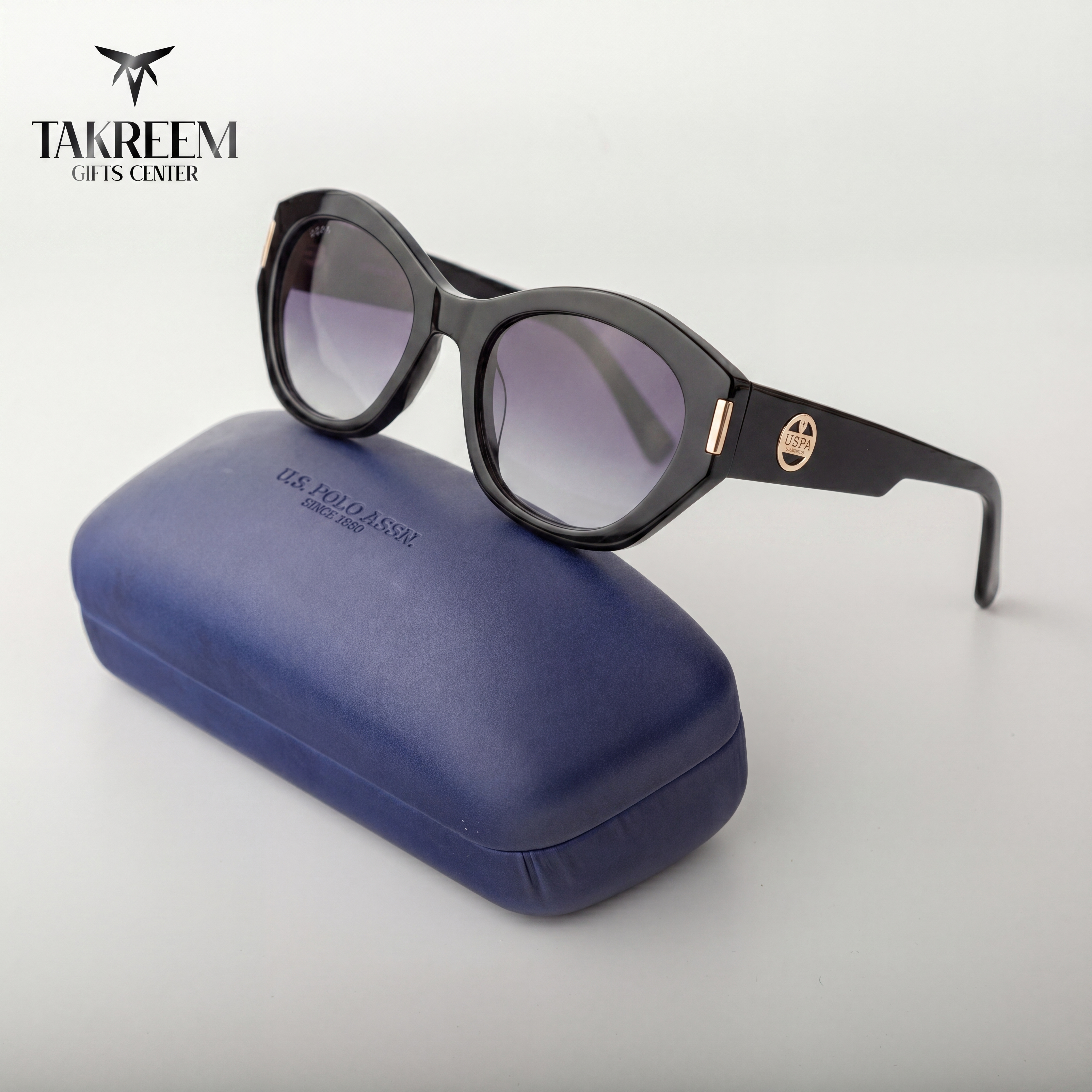 Black sunglasses with gradient lenses on a blue case, branded 'Takreem Gifts Center'.