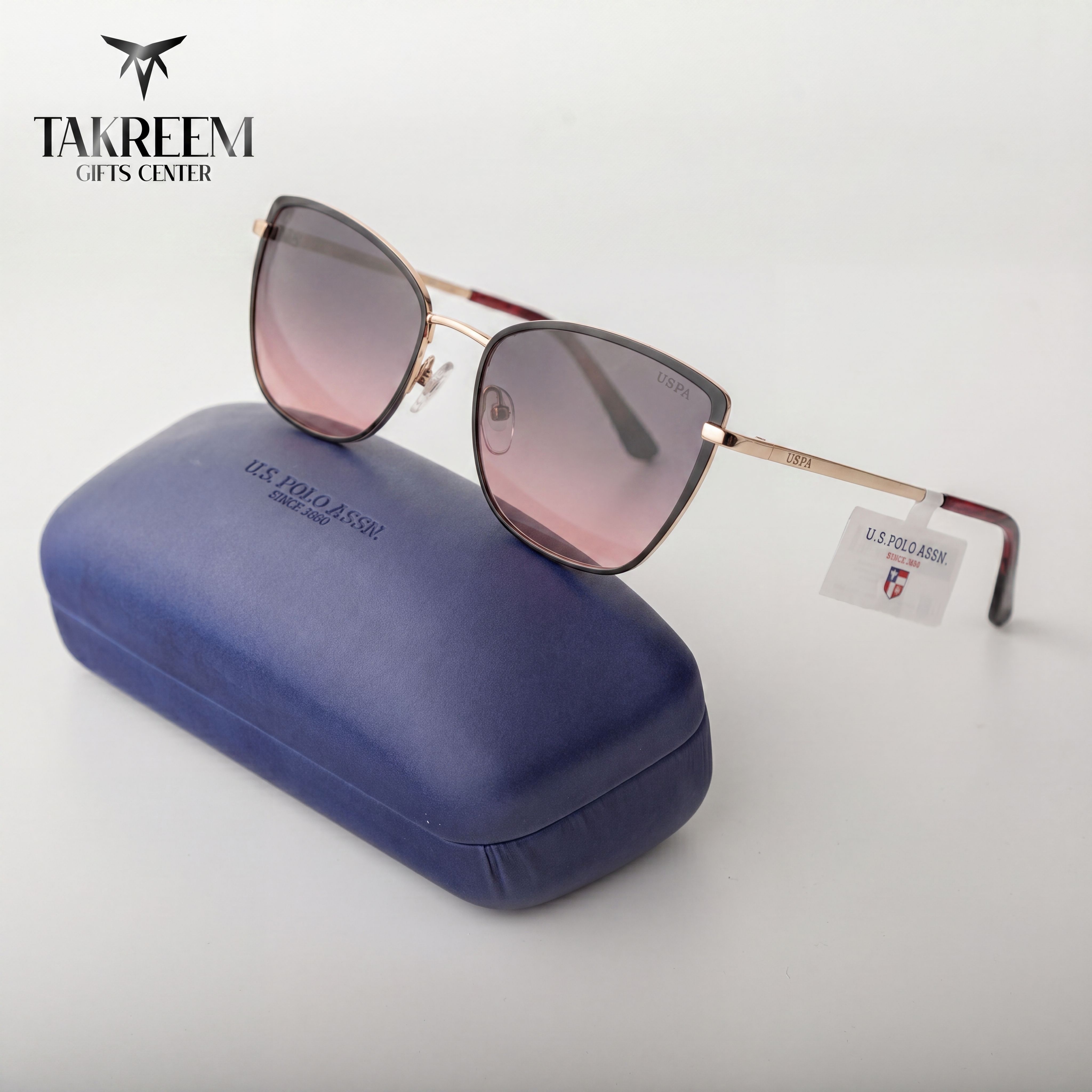 Sunglasses with pink gradient lenses and gold frame on a blue case, brand 'Takreem' visible.