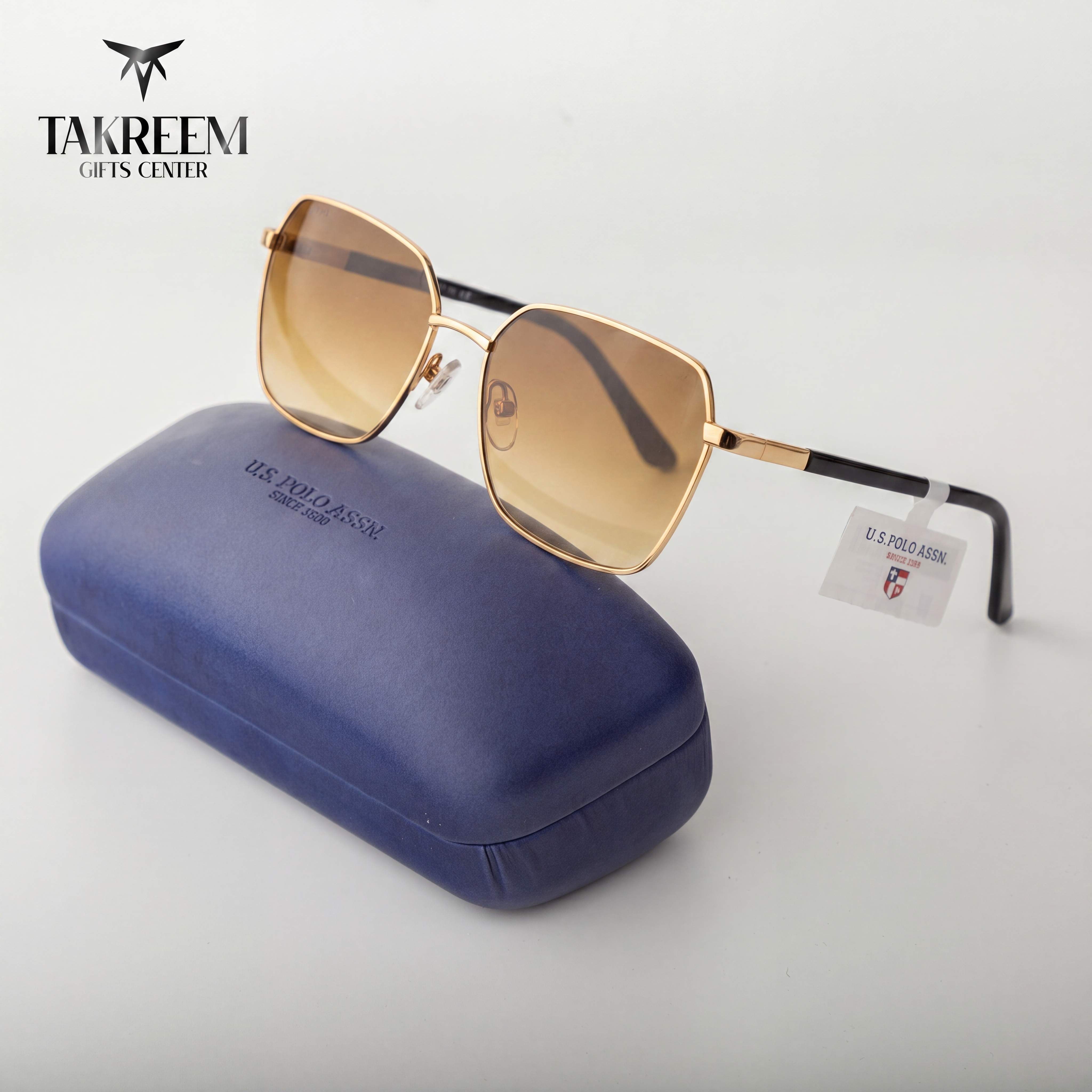 Gold sunglasses with a blue case on a white background, featuring the Takreem Gifts Center logo.
