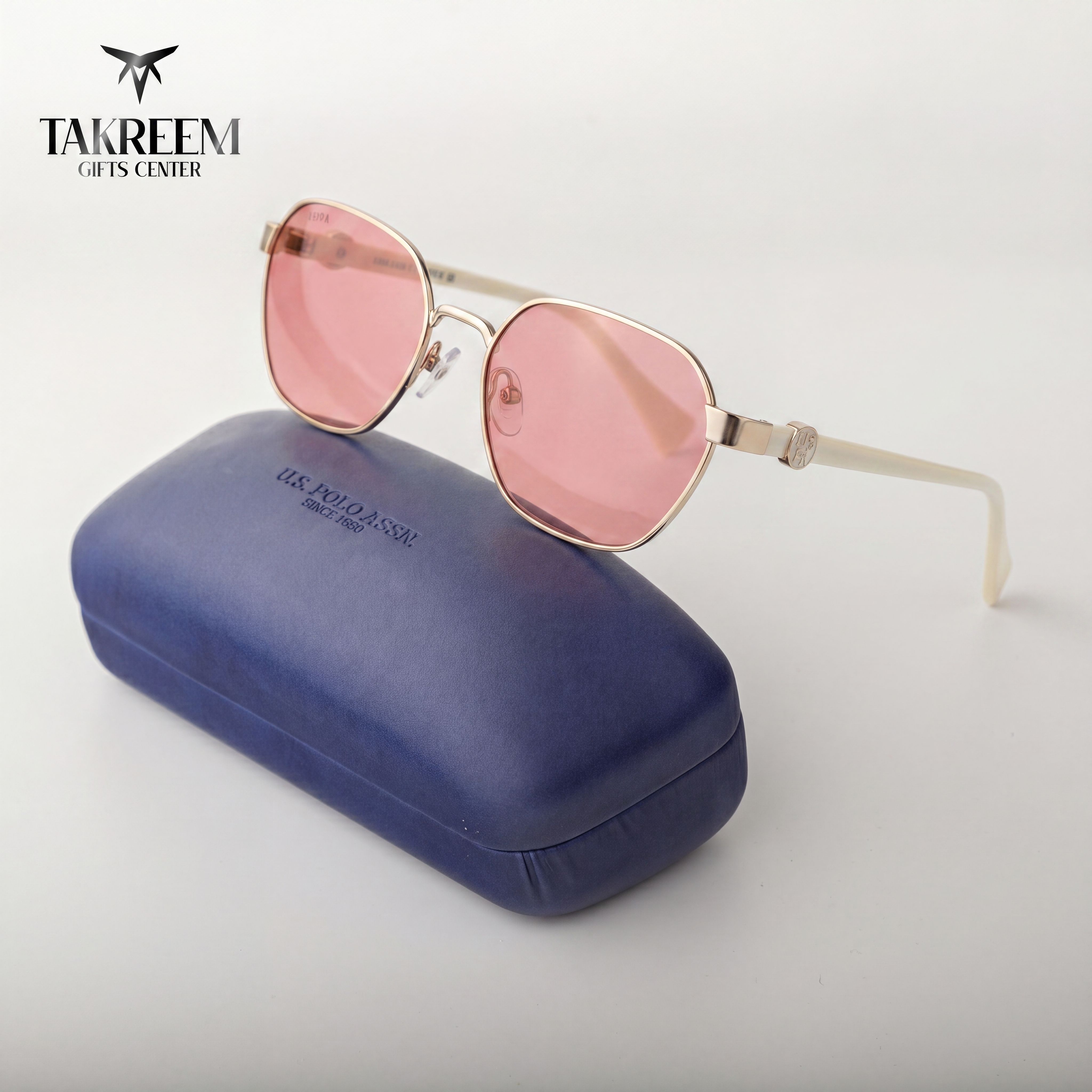 Pink sunglasses with gold frame on a blue case, brand 'Takreem' visible.