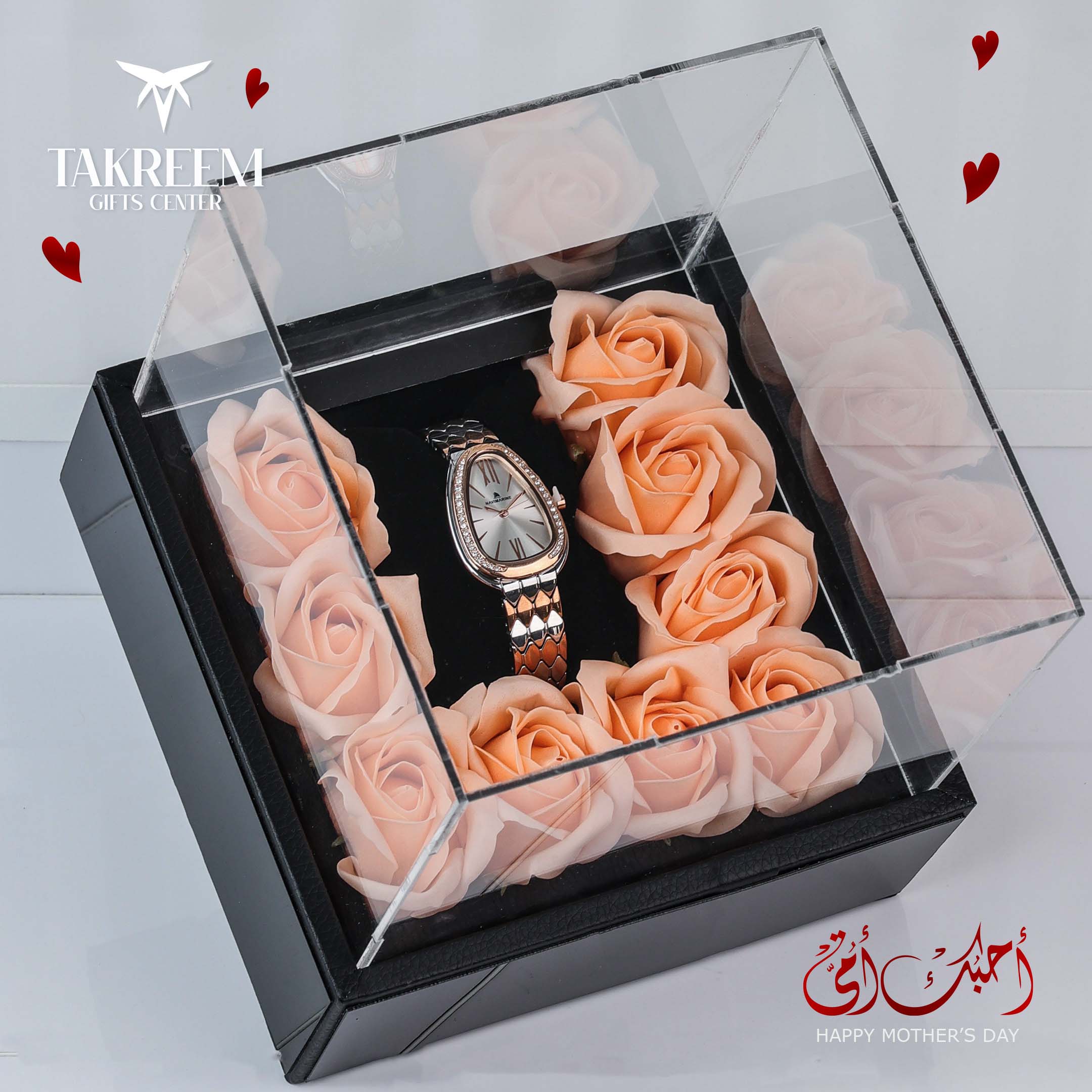 Watch surrounded by pink roses in a clear box with 'Takreem Gifts Center' branding.