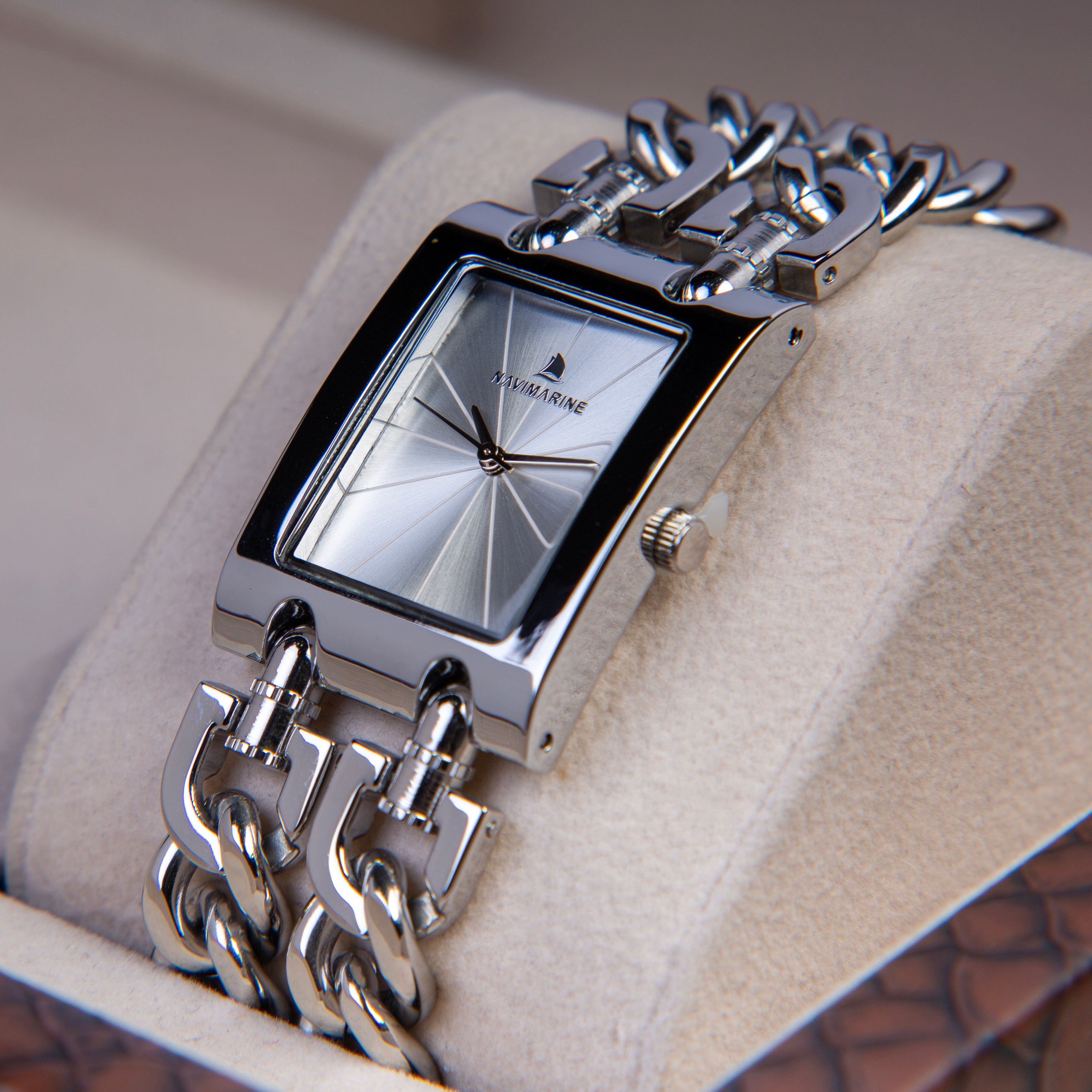 Silver wristwatch with chain design on a beige cushion
