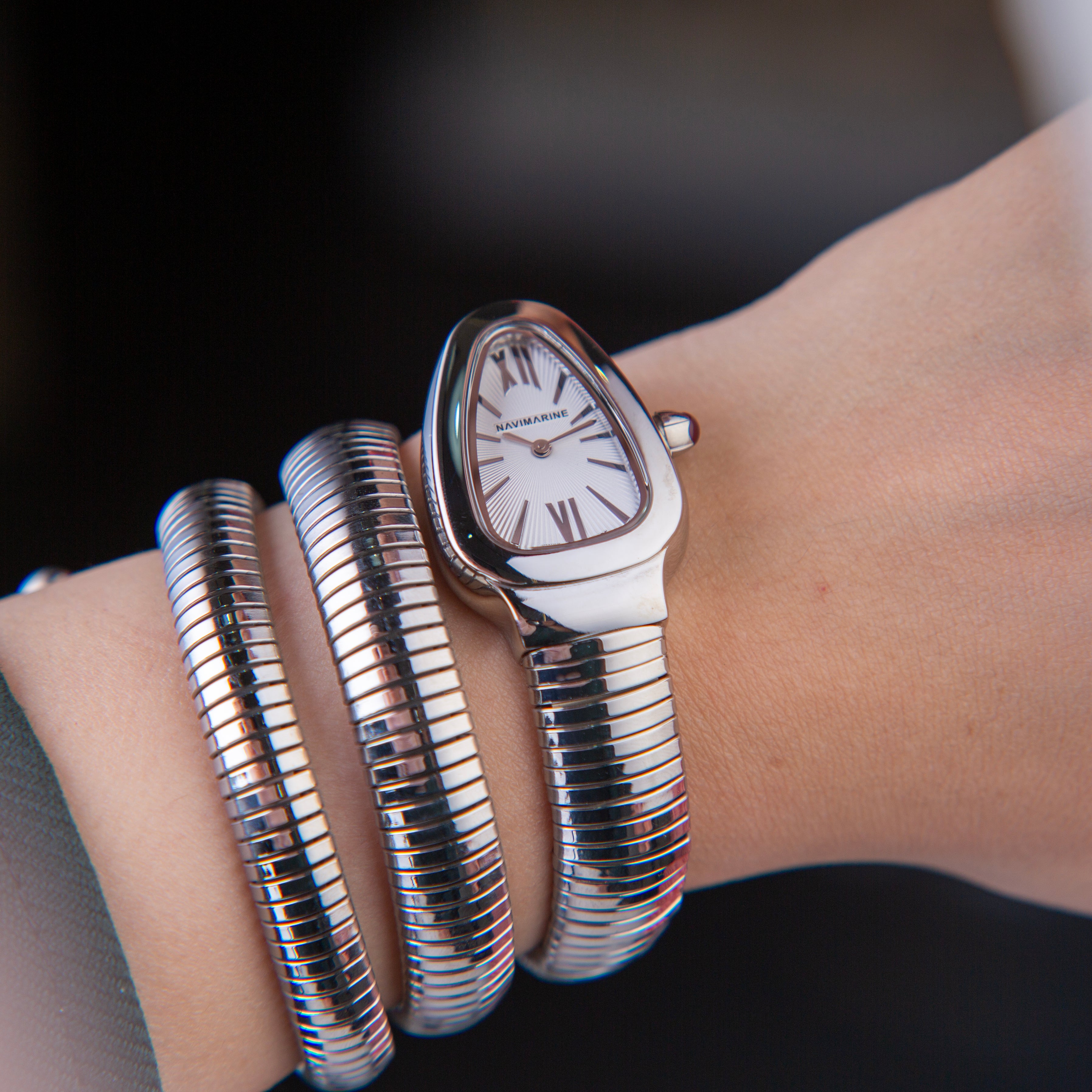 Silver watch with snake-like band worn on a wrist against a dark background
