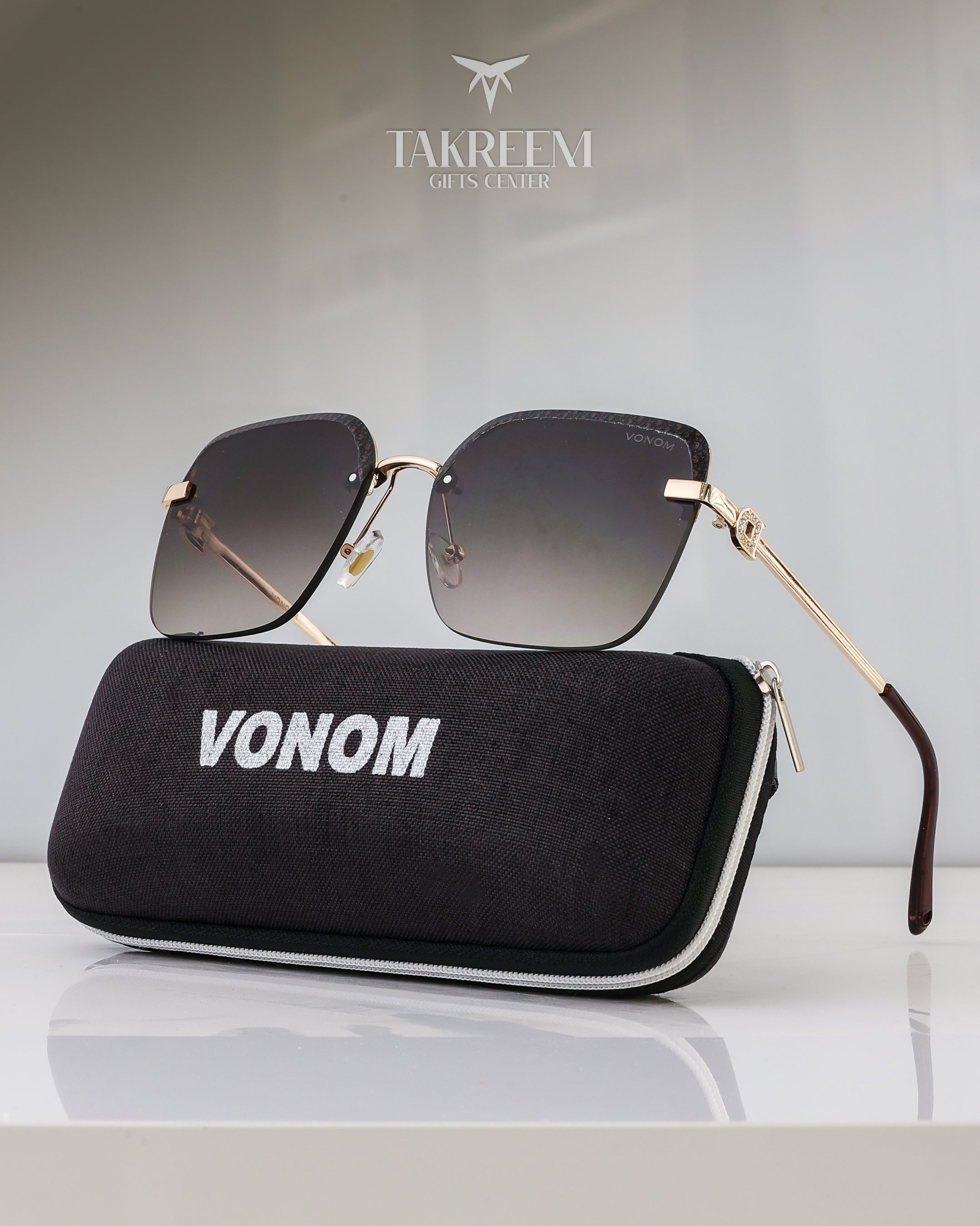 Sunglasses with gold frame and dark lenses on a black case labeled 'VONOM' with 'Takreem' brand logo.