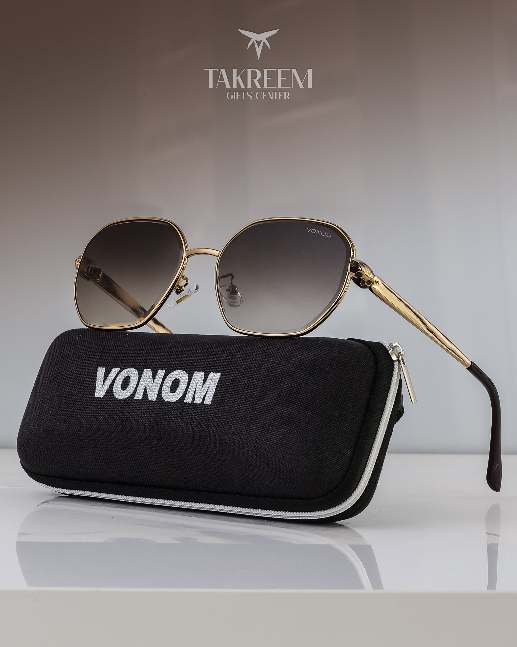 Sunglasses with gold frame and gradient lenses on a black case labeled 'VONOM' with 'Takreemi Gifts Center' branding in the background.