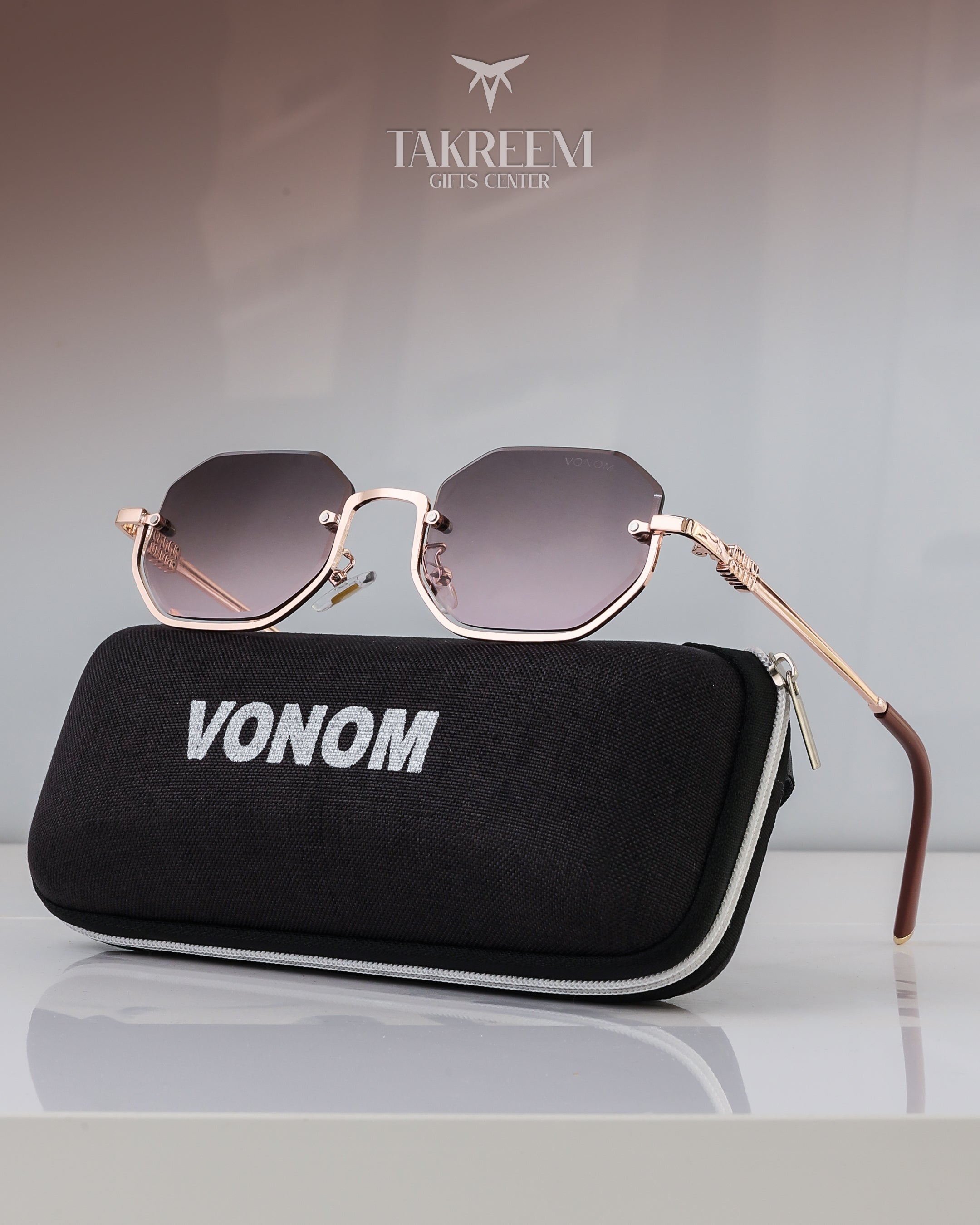 Sunglasses with gold frame and dark lenses on a black case labeled 'VONOM' with 'Takreem Gifts Center' logo in the background.