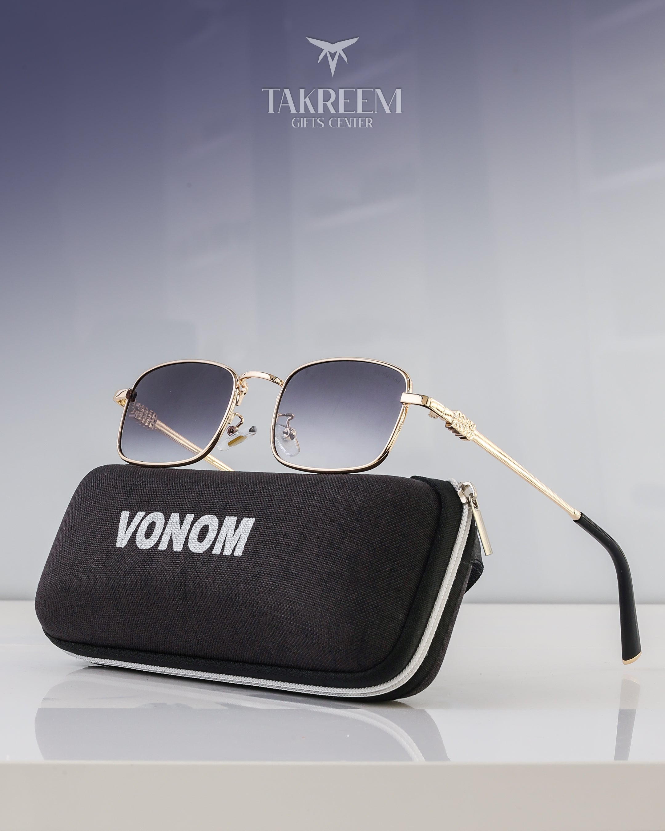 Gold-framed sunglasses with a black case labeled 'VONOM' on a reflective surface.