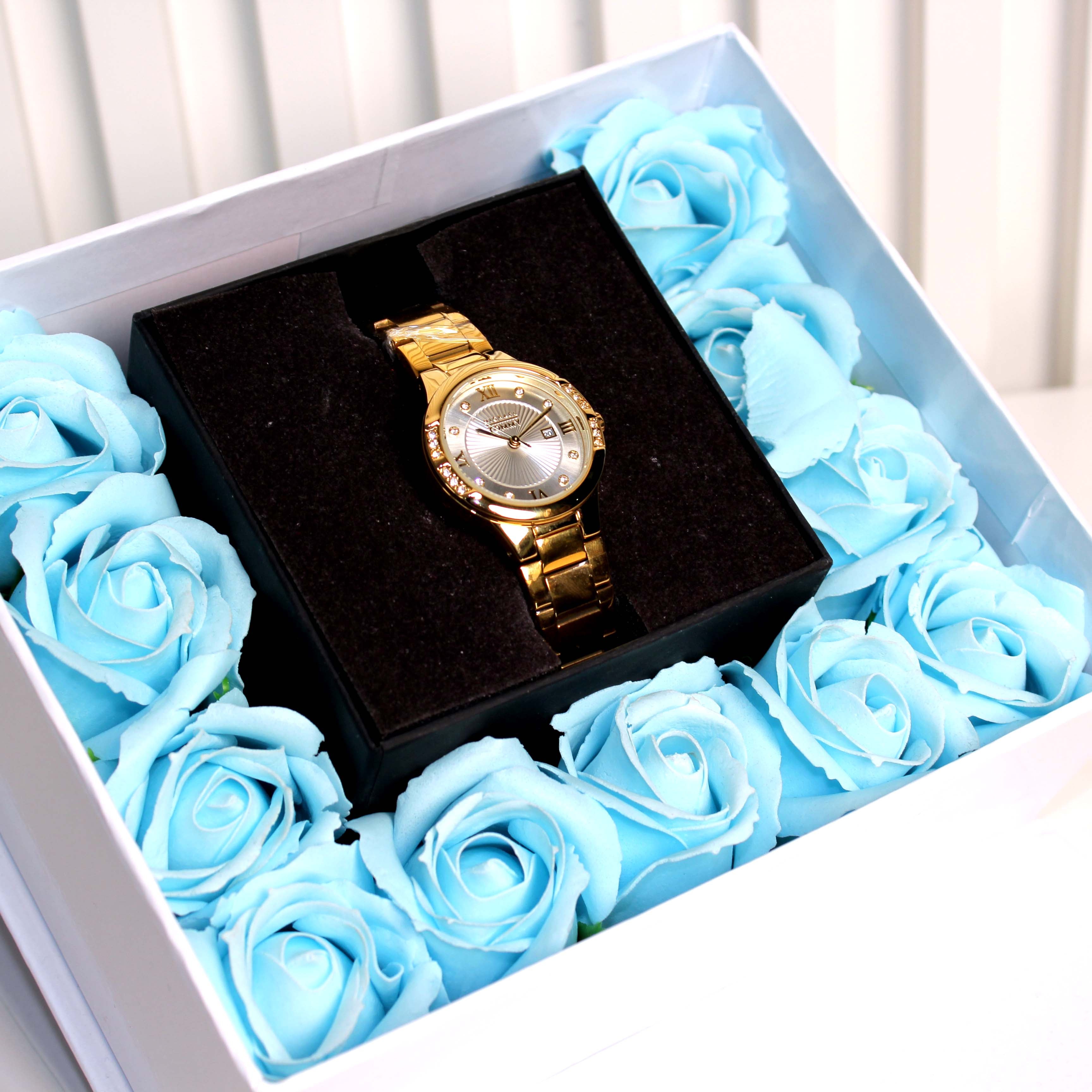 Gold watch in a box surrounded by blue roses on a white background