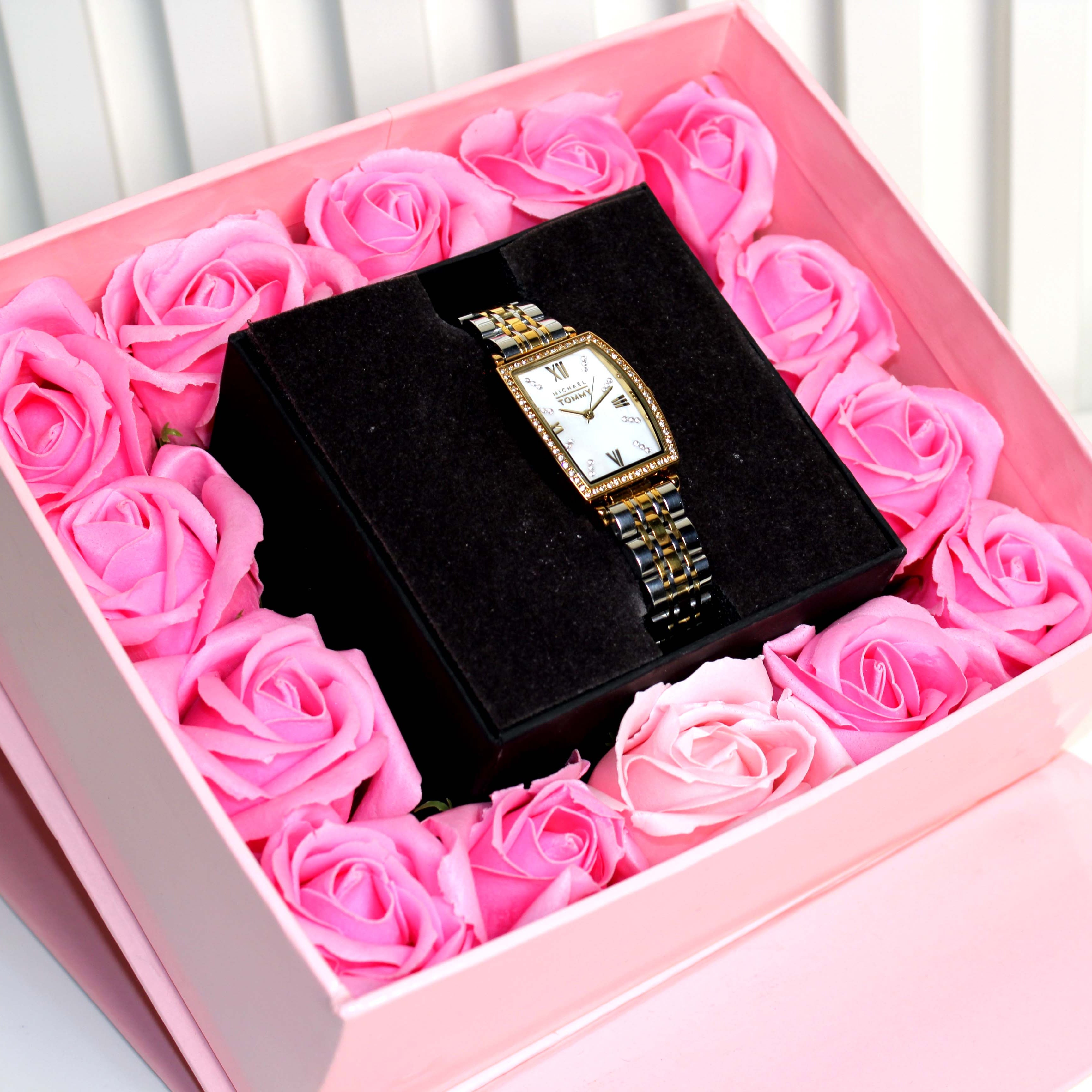 Watch in a box surrounded by pink roses on a white background