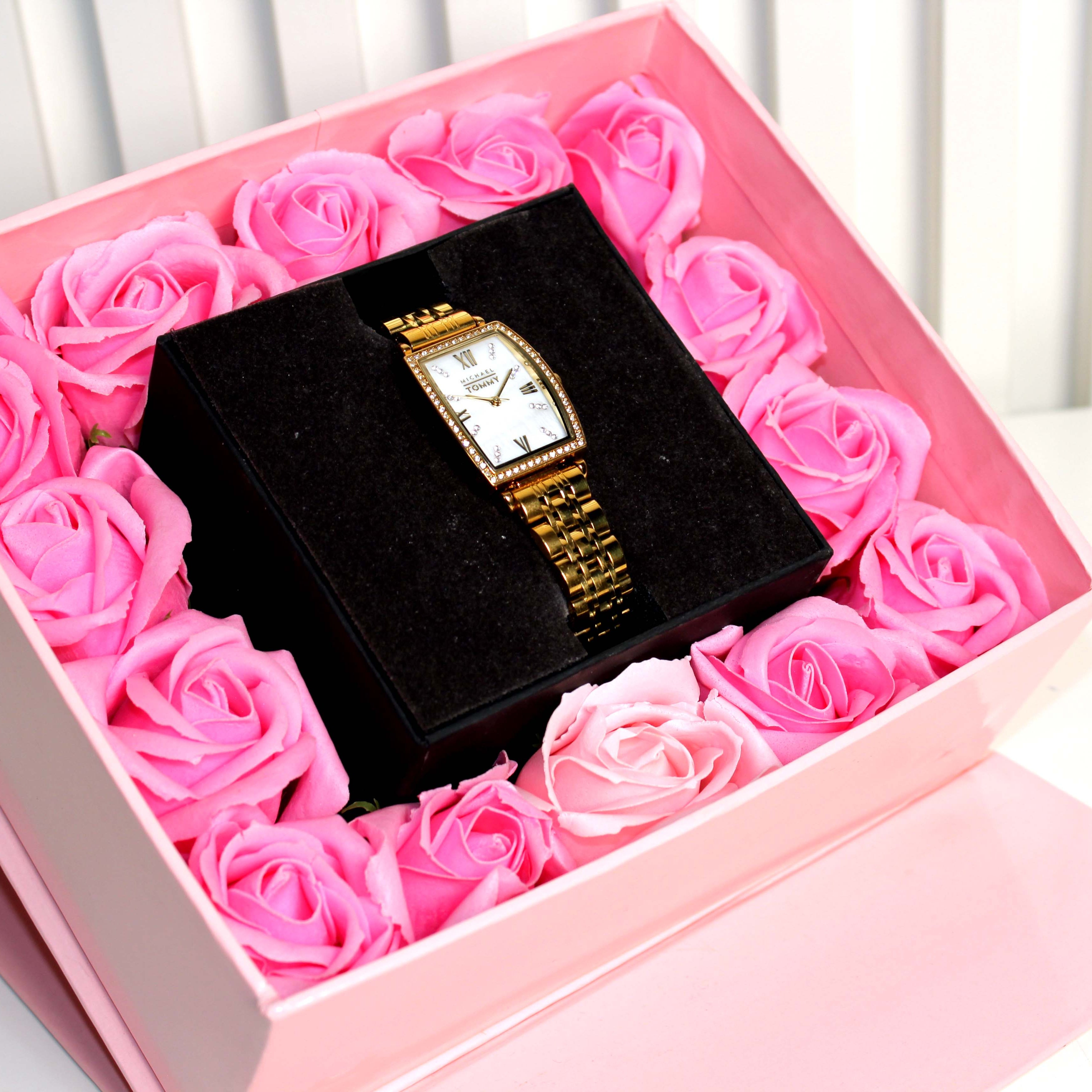 Gold watch in a box surrounded by pink roses