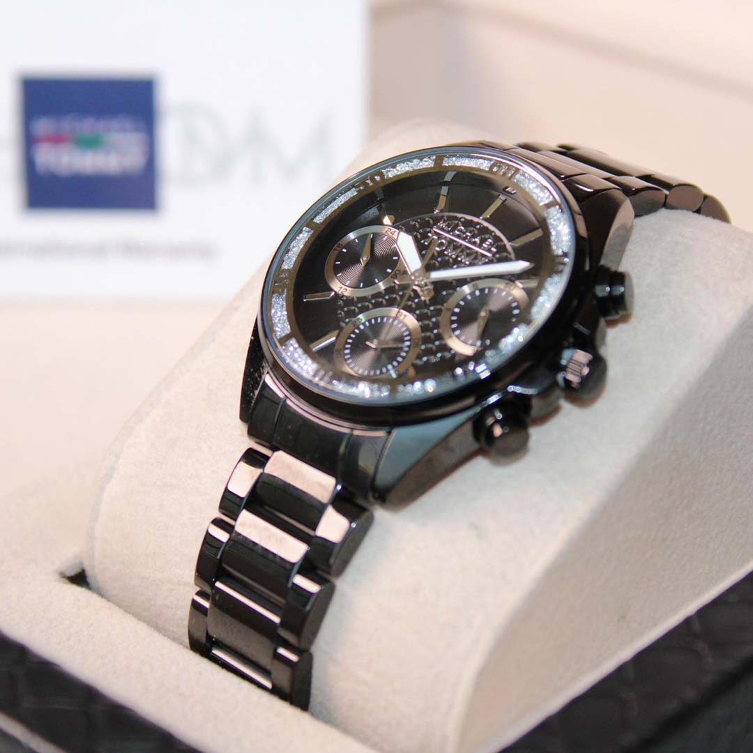 Black wristwatch with detailed face on a white cushion, brand logo in the background
