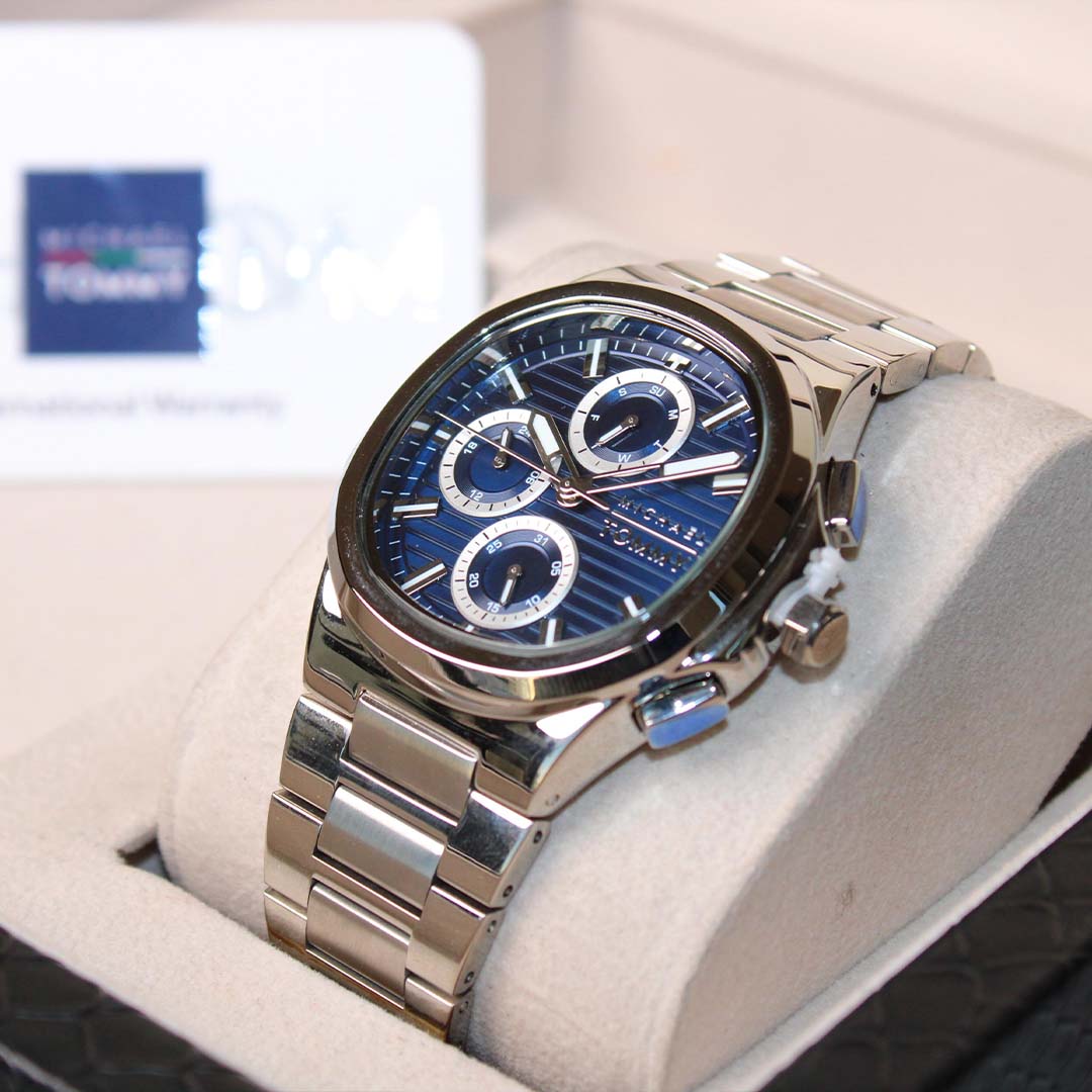 Silver watch with blue face on a white cushion, brand logo in the background
