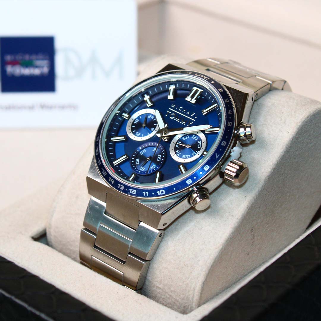 Silver watch with blue face on a white cushion, brand logo visible in the background