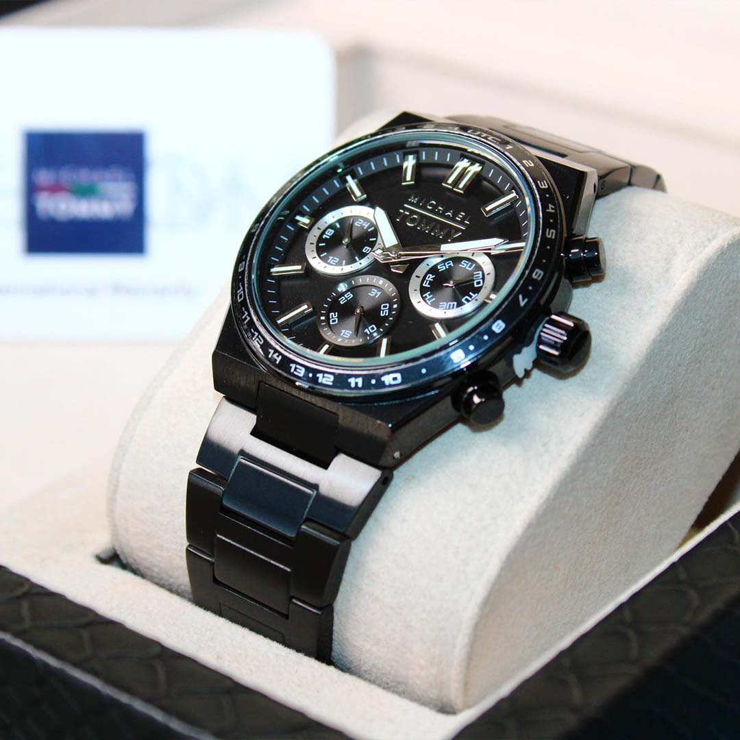 Black wristwatch with detailed face on a white cushion, brand logo in the background