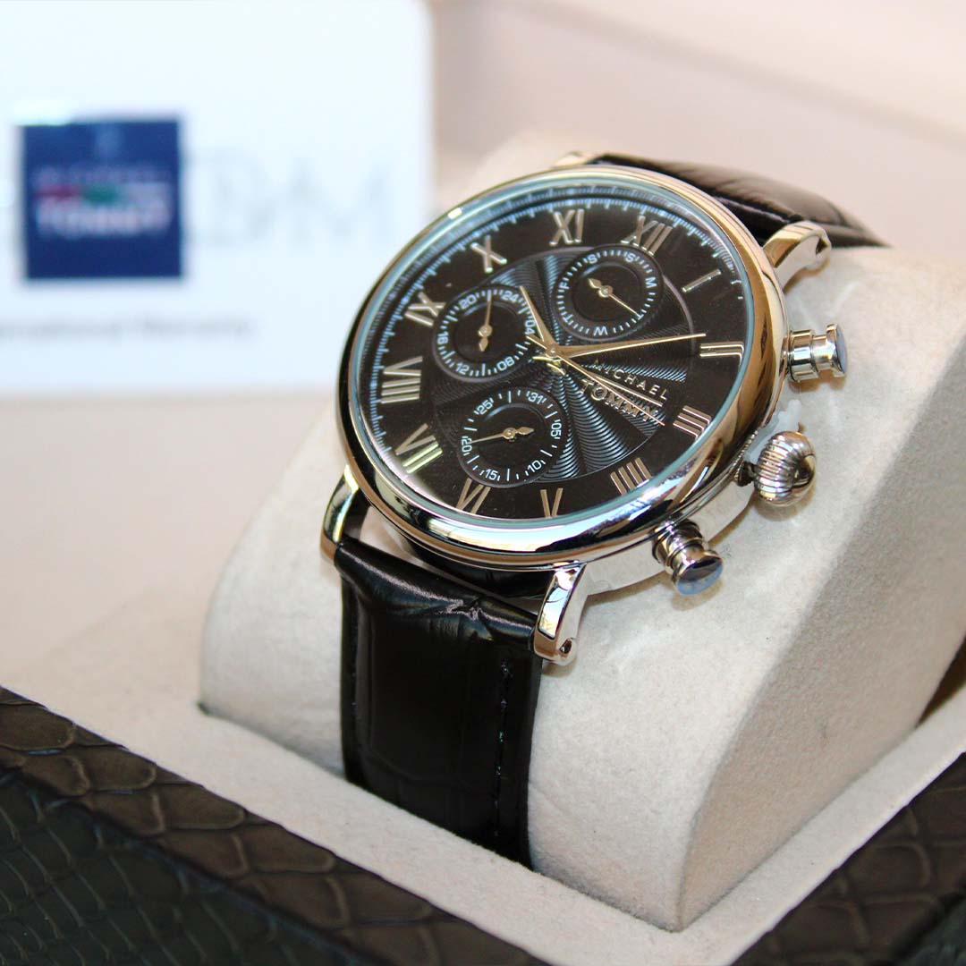 Luxury watch with black face and leather strap on a white cushion